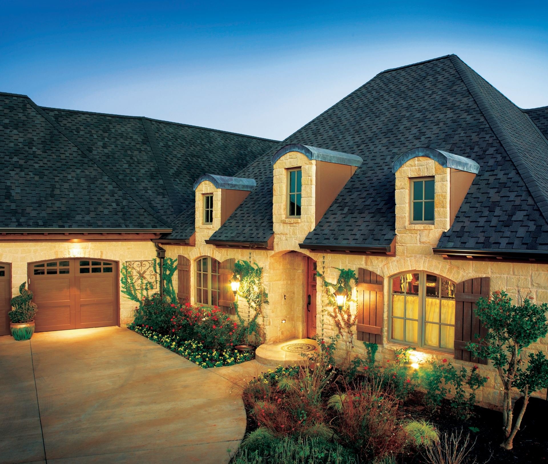 A modern house with a black shingled roof and a driveway with a wooden garage door