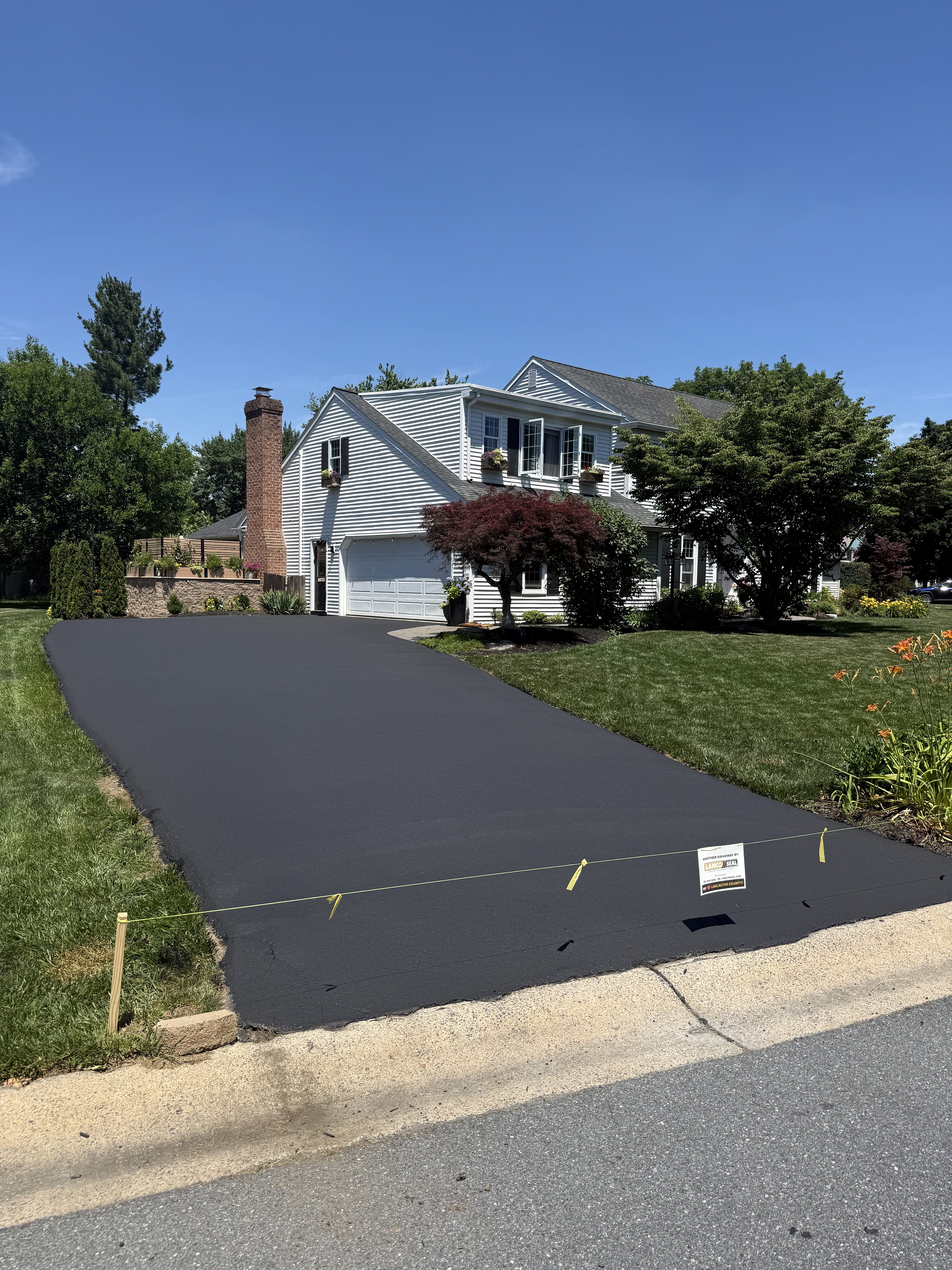 A newly paved driveway in front of a white house with a brick chimney