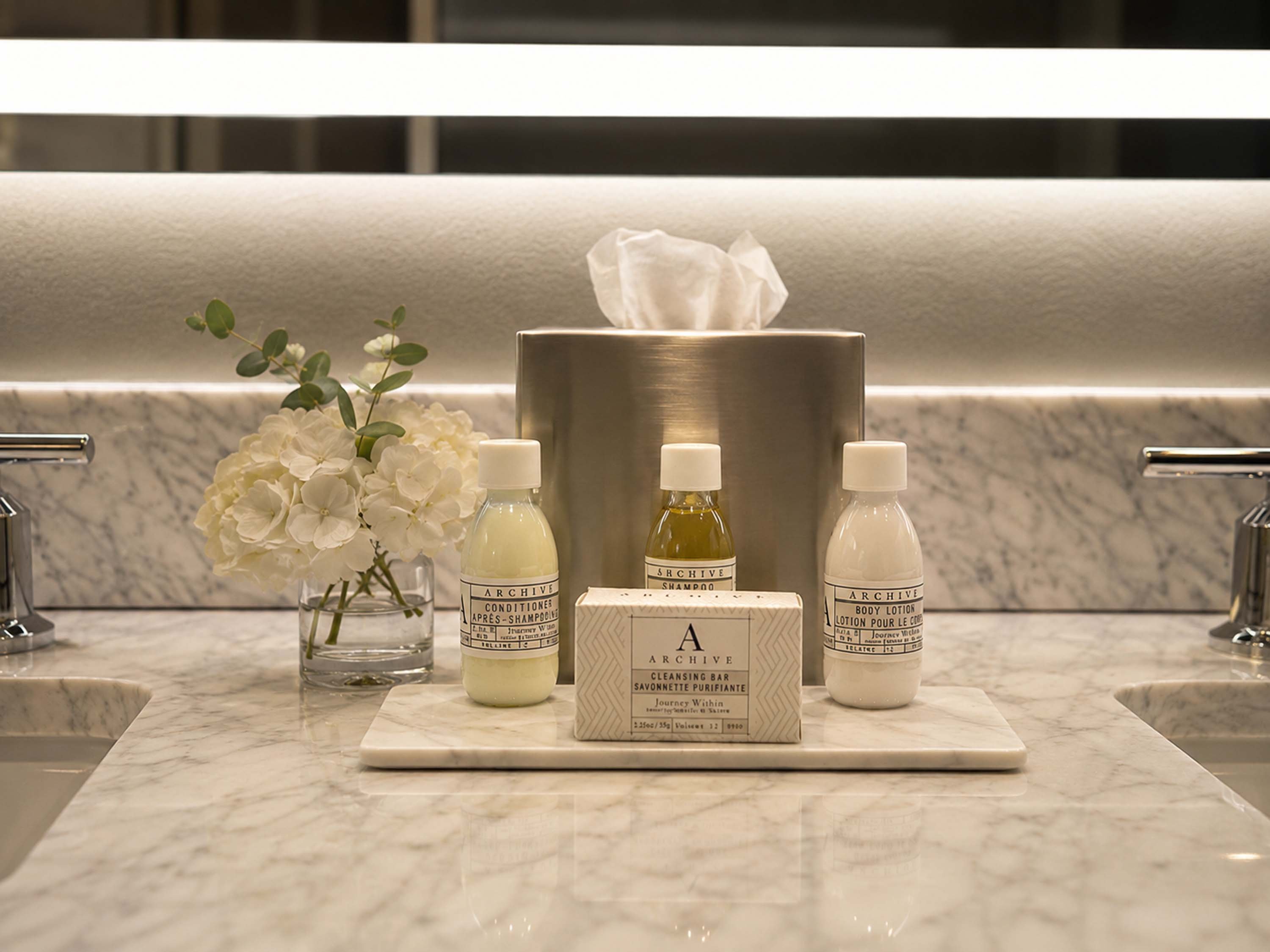 A bathroom vanity with a marble countertop, tissue box, and Archive brand products