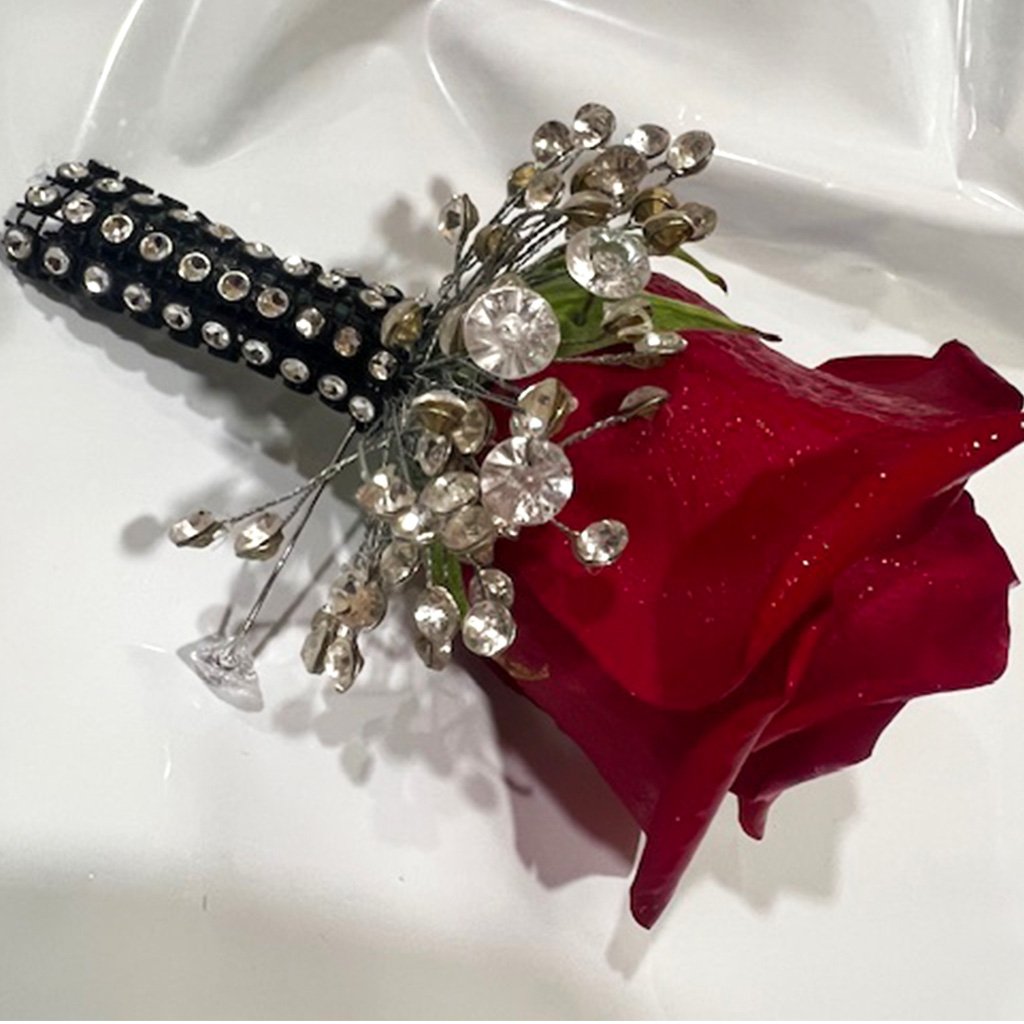 A red rose with a silver brooch and crystals on a white cloth