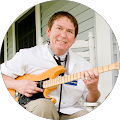A man in a white lab coat and stethoscope plays an electric guitar on a porch.