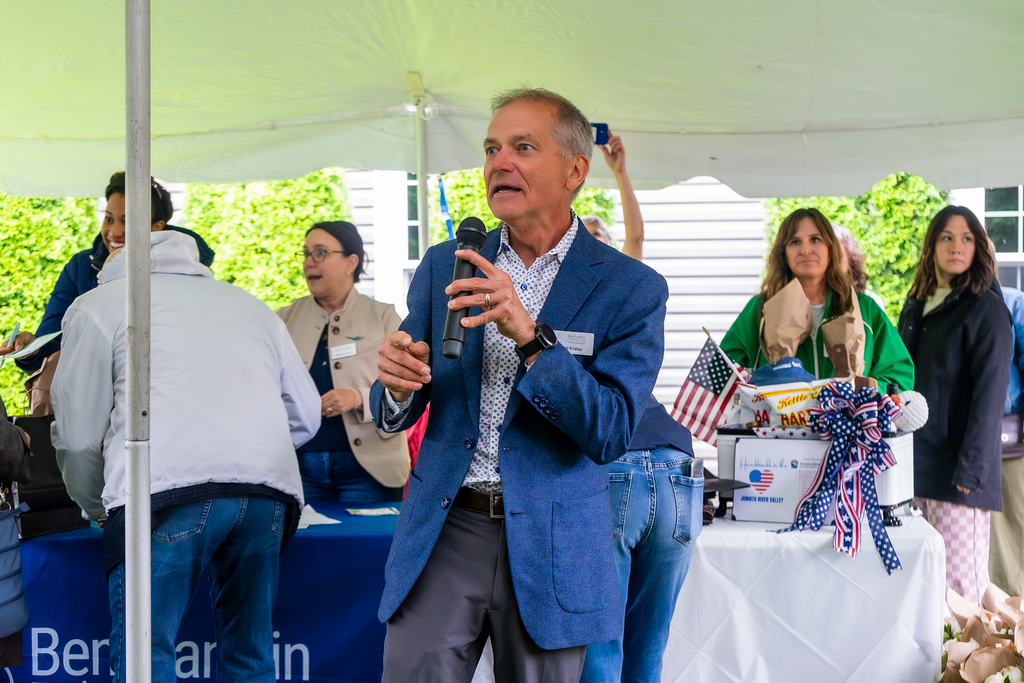 Todd Erdley speaking into a microphone at an outdoor event with a crowd of people