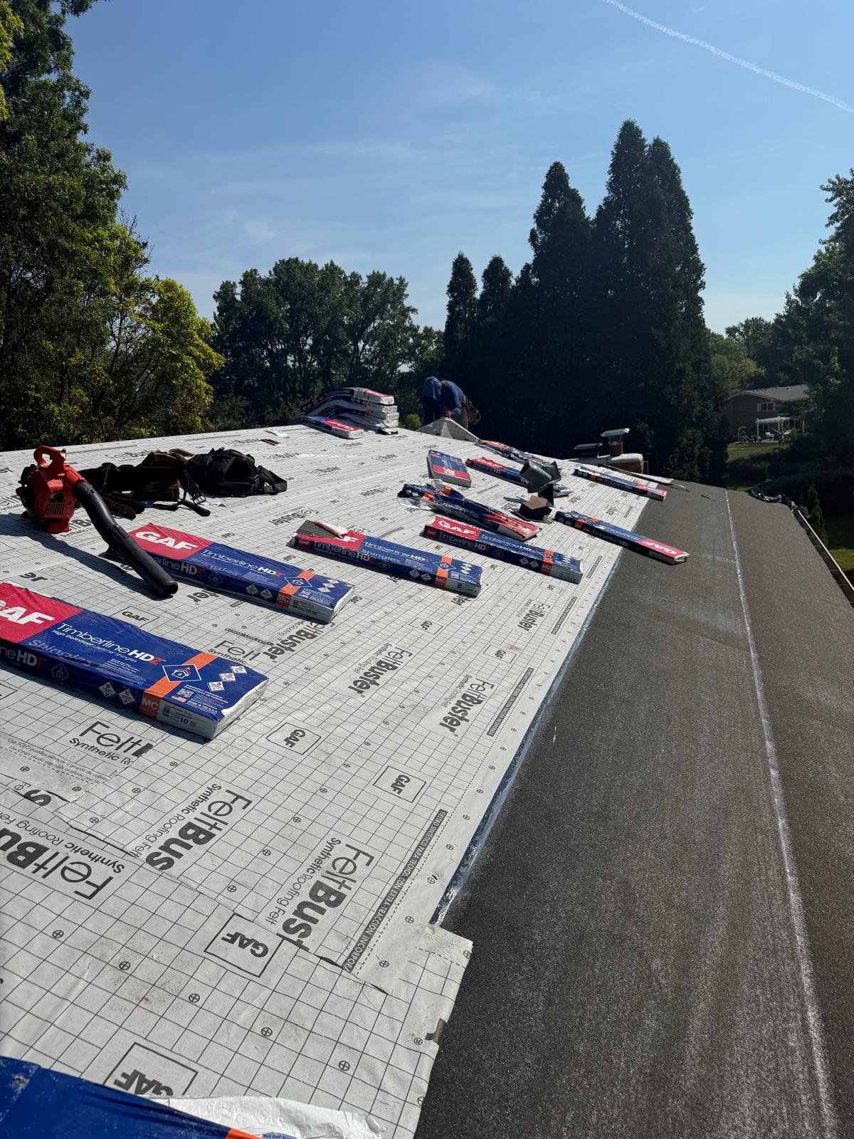 Roofing materials and tools on a roof under a clear blue sky