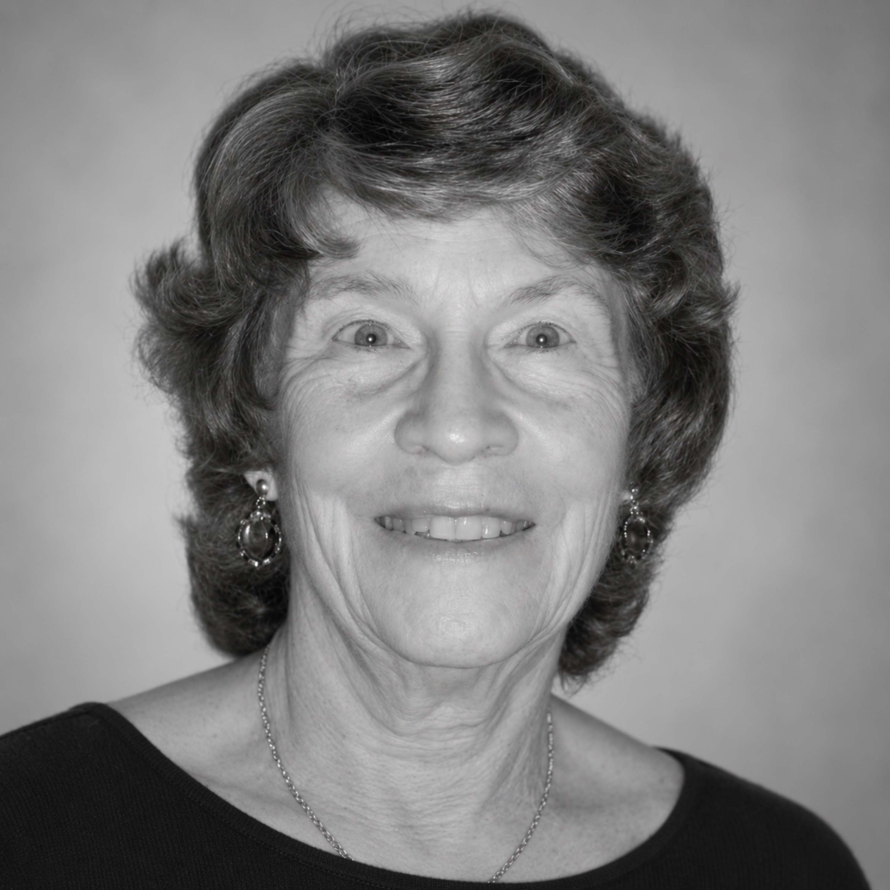 A black and white headshot of an older woman with short hair, smiling