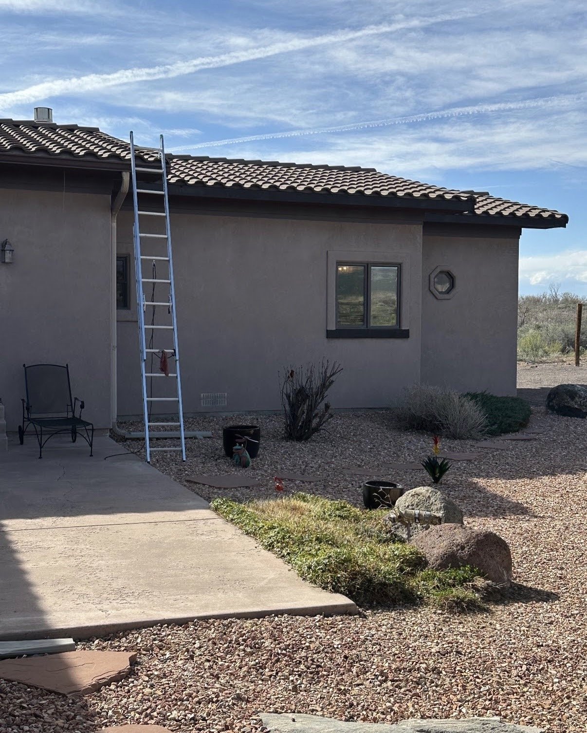A house with a ladder leaning against it and a patio area with a chair and plants
