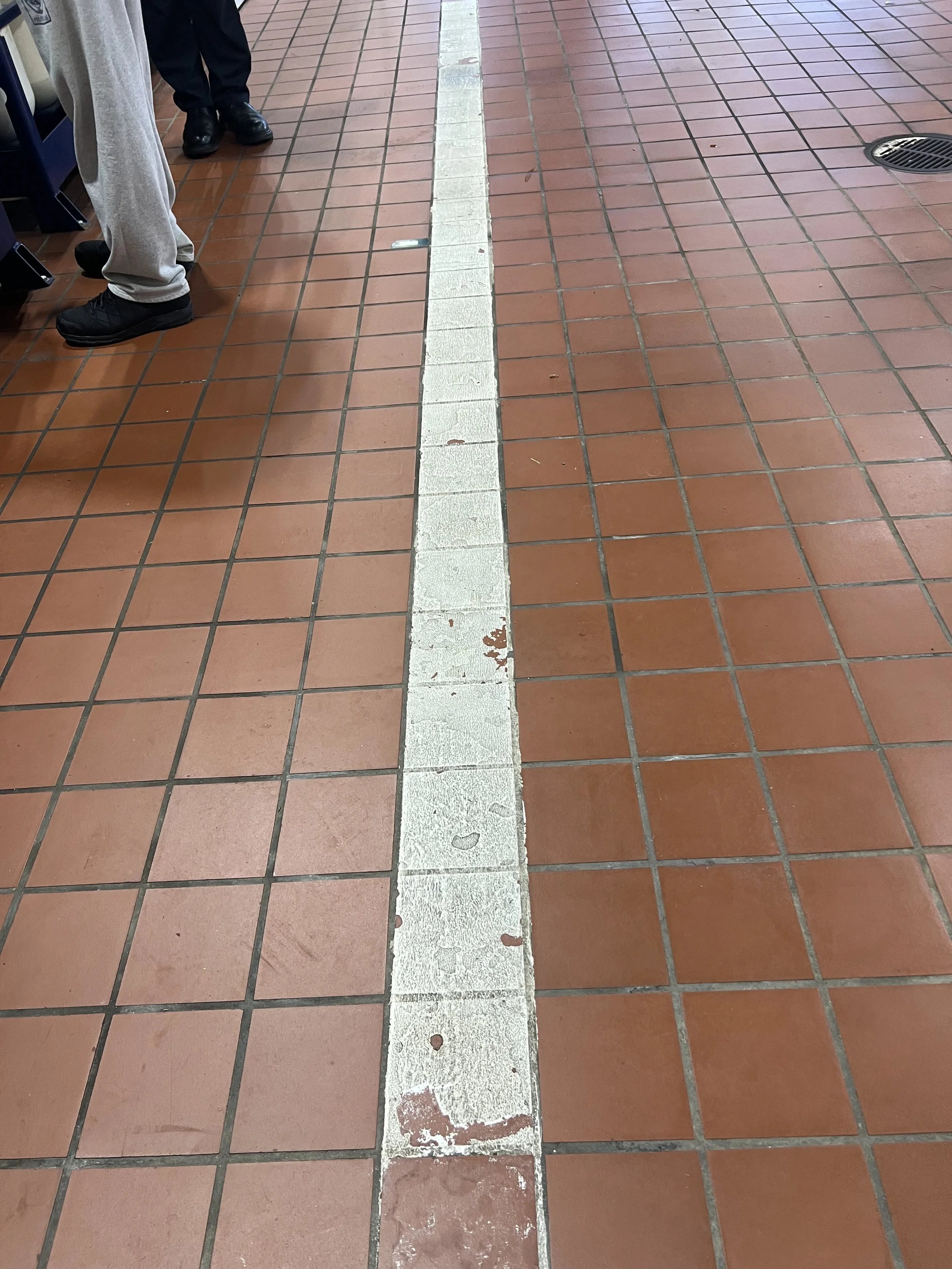 A white line on a brown tiled floor with people standing nearby
