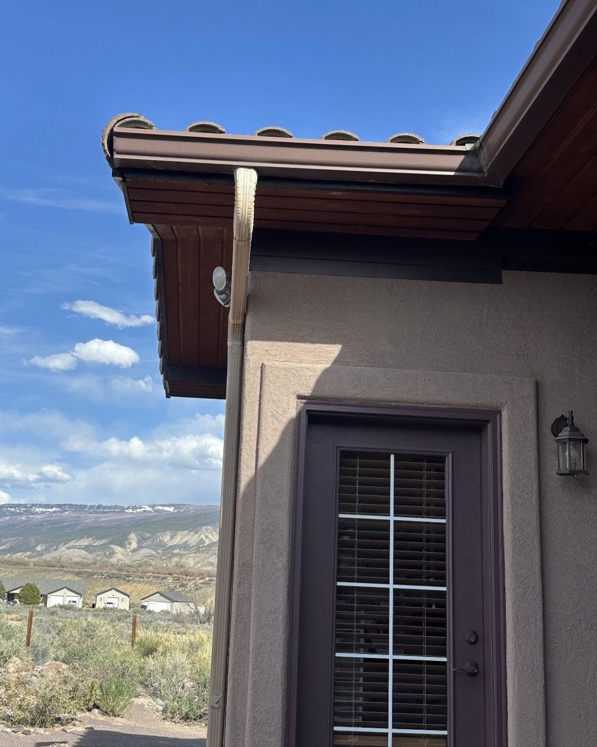 A house exterior with a brown door and a gutter on a sunny day