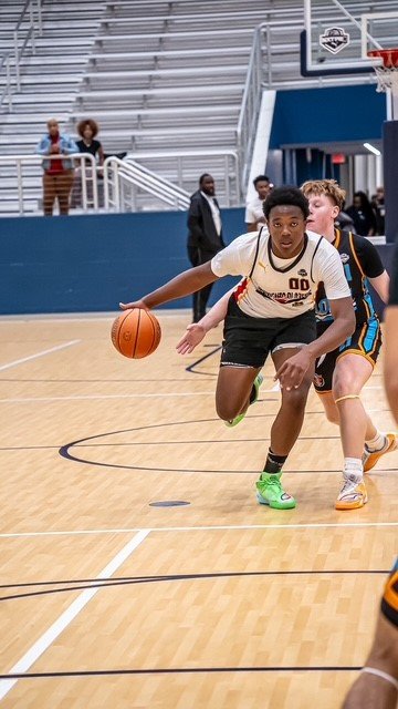 Zyire Wells, a basketball player in white, dribbles the ball on an indoor court.