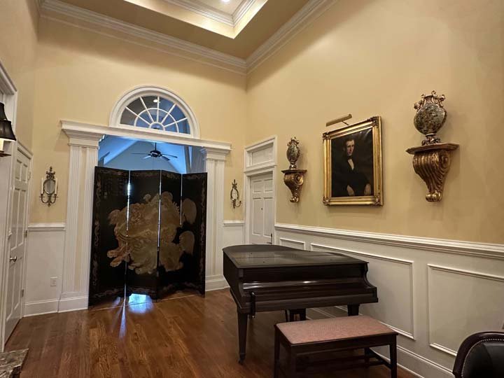 A grand piano in a room with a wooden floor, a ceiling fan, and a decorative screen