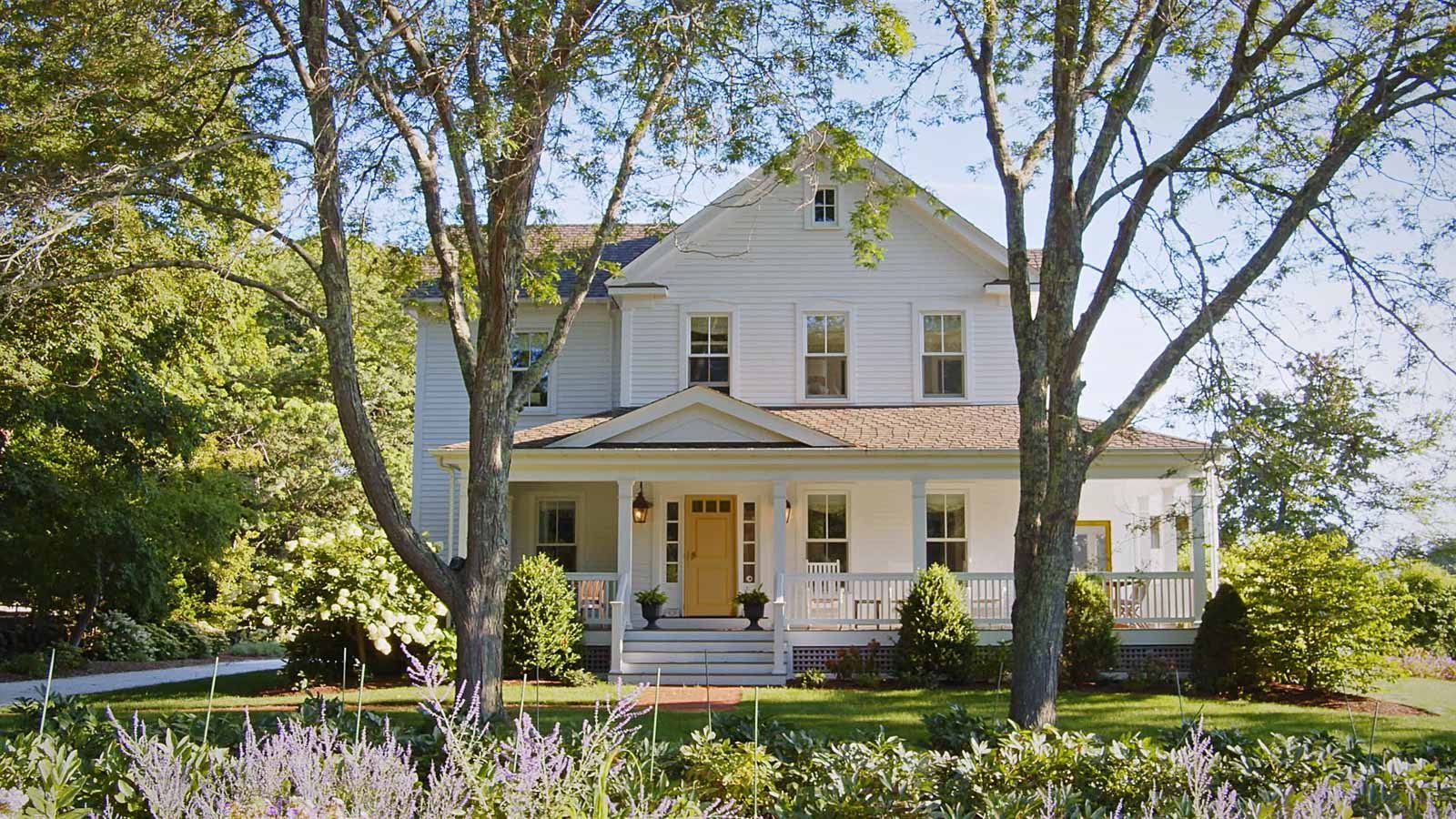 White two-story lake house with a porch and yellow door surrounded by trees in Lake Ariel, Pennsylvania