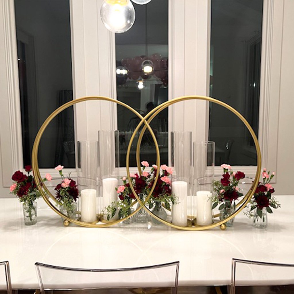 Two gold candle holders with candles and flowers on a white table