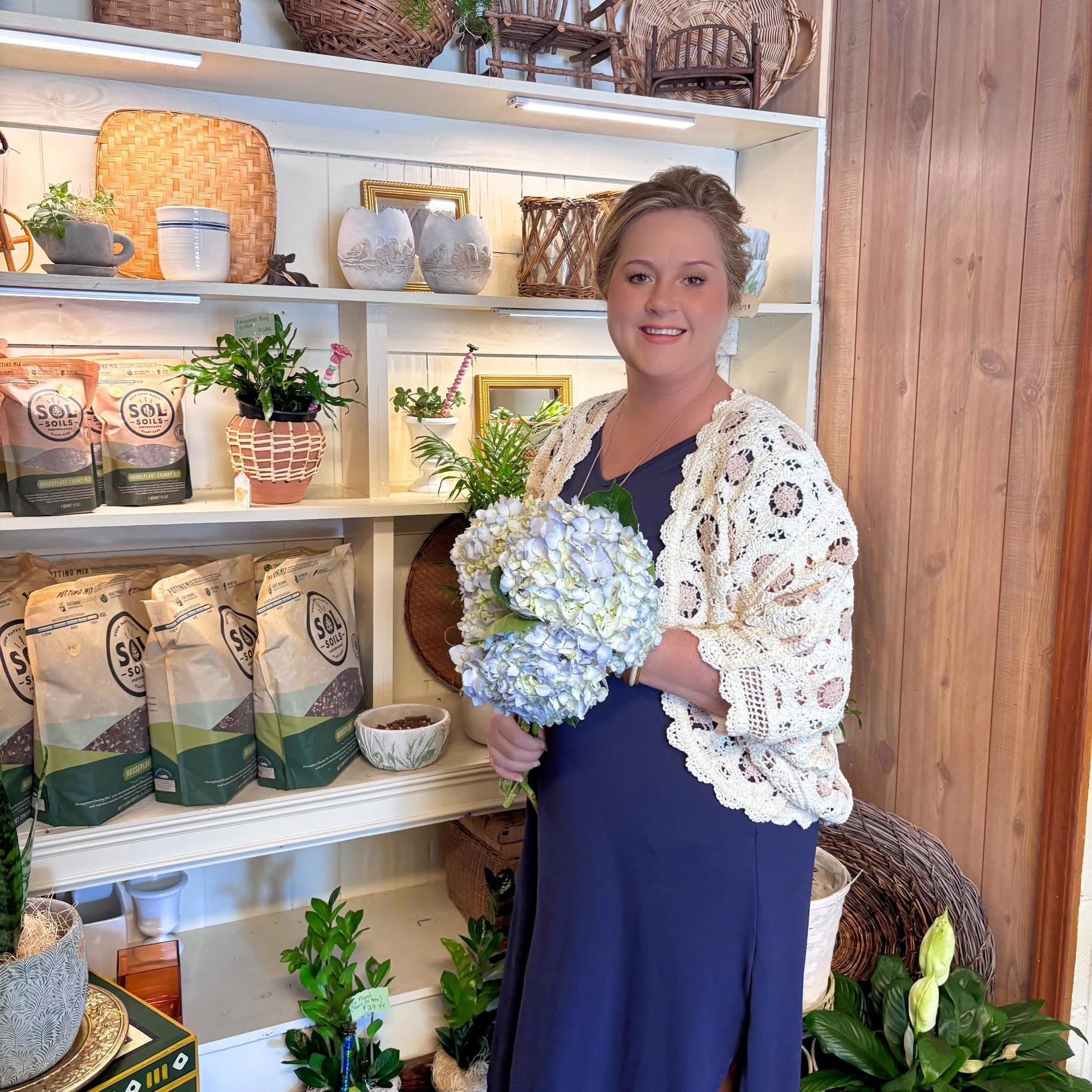 A woman in a blue dress holding a bouquet of blue hydrangeas in a shop