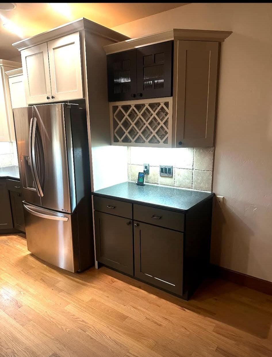 A modern kitchen with a stainless steel refrigerator, dark cabinets, and a wine rack above the counter