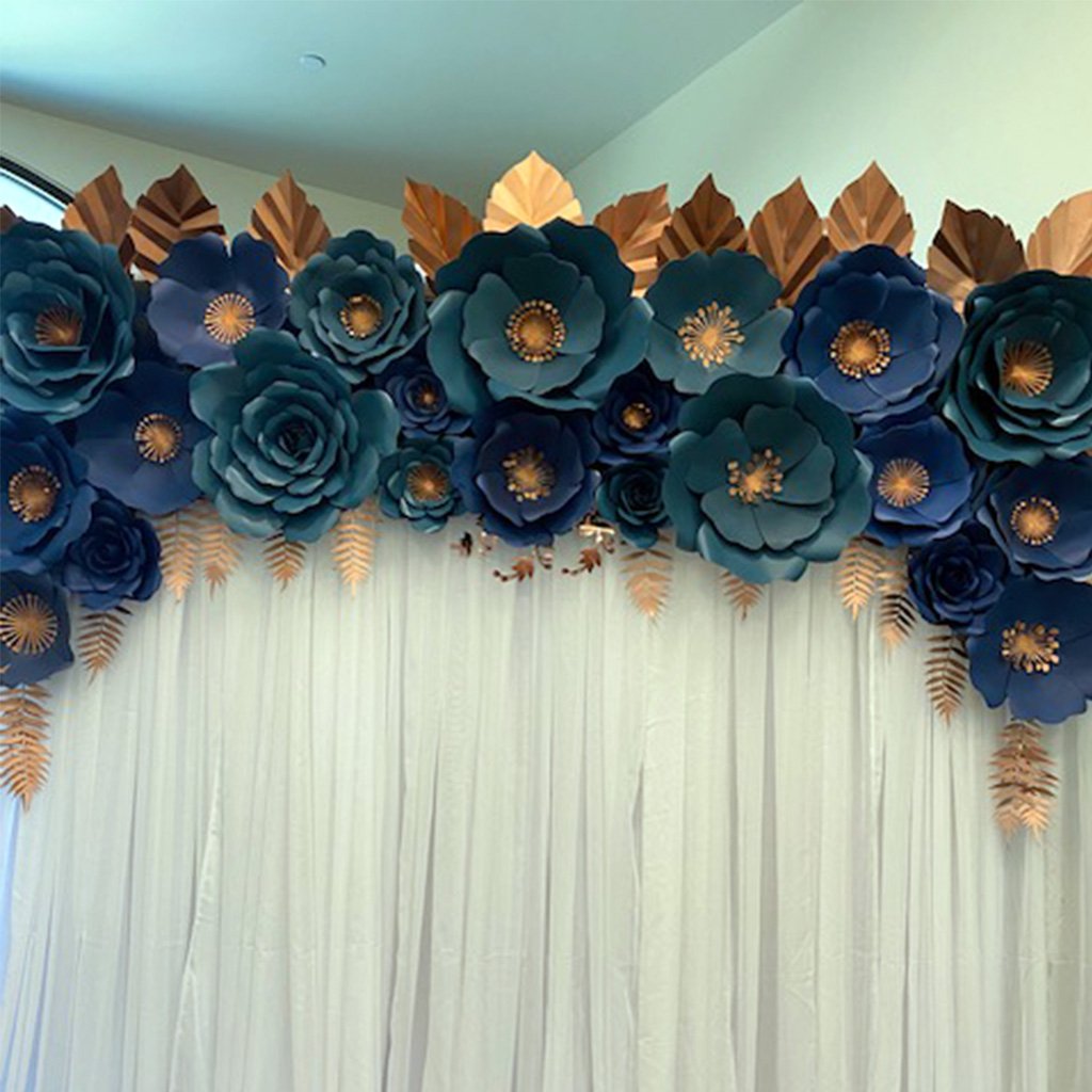 A white backdrop adorned with blue paper flowers and gold leaves