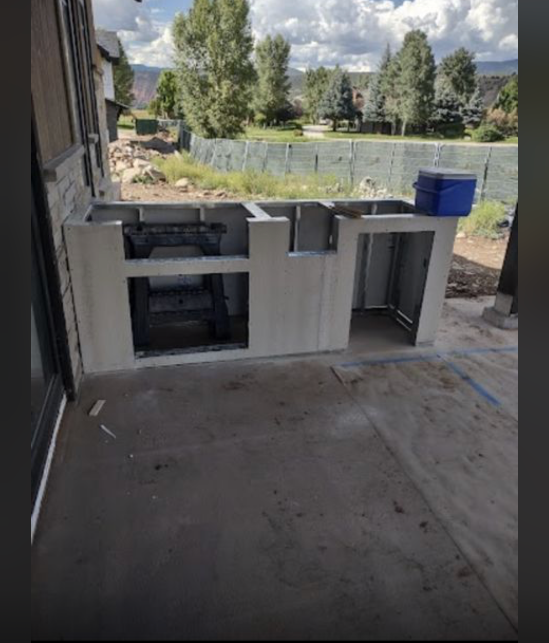 A concrete outdoor kitchen island under construction with a blue cooler on top
