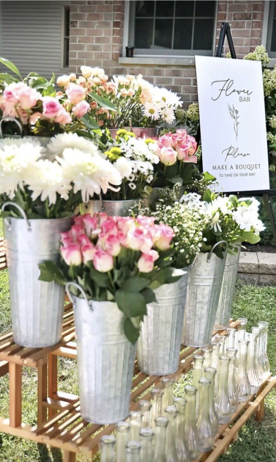 A flower bar with various flowers in buckets and vases on a wooden stand