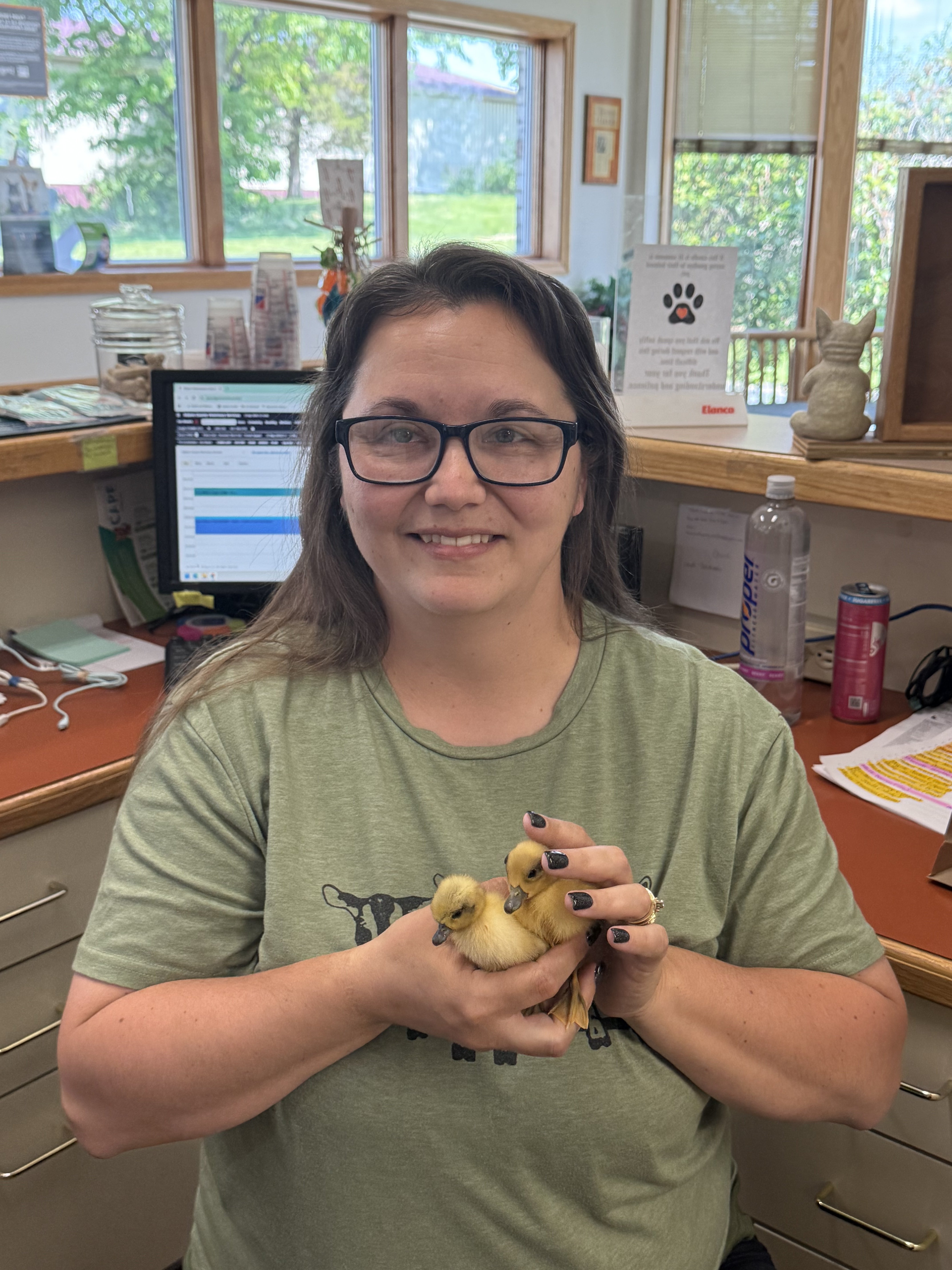 A woman holds two ducklings in her hands while smiling at the camera