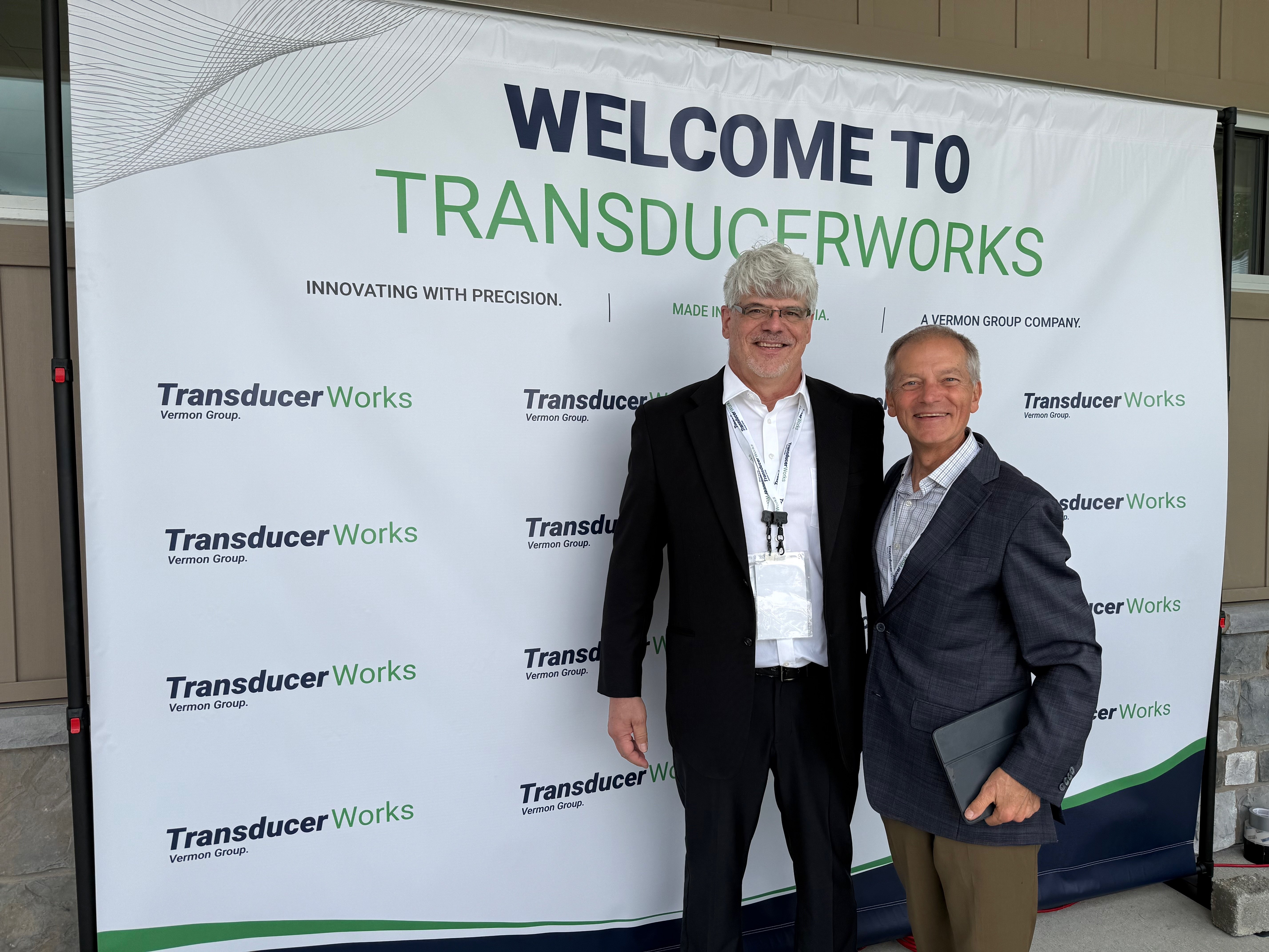 Two men standing in front of a Transducer Works banner at an event