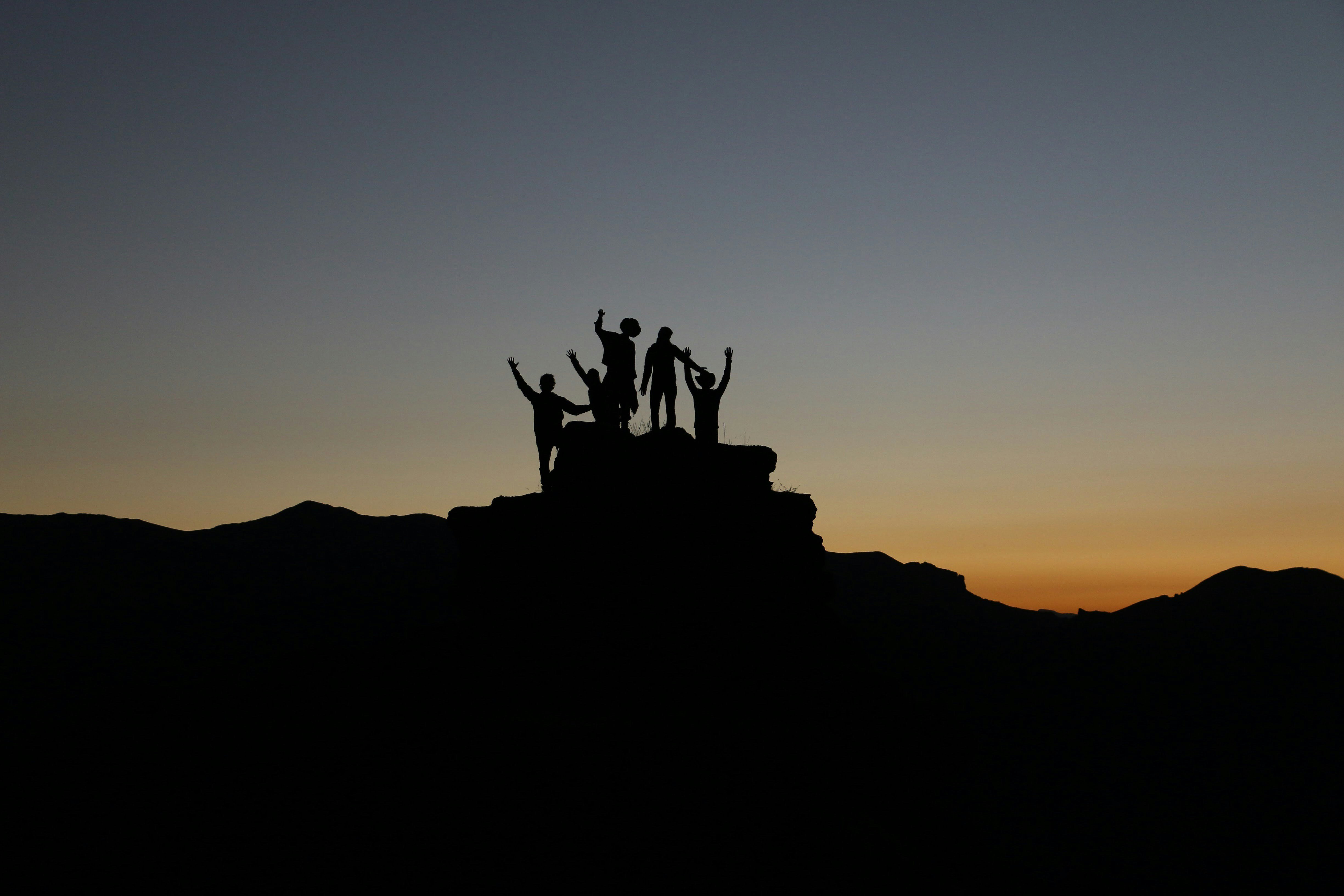 Silhouette of hikers raising their arms in victory on a mountain peak at sunset