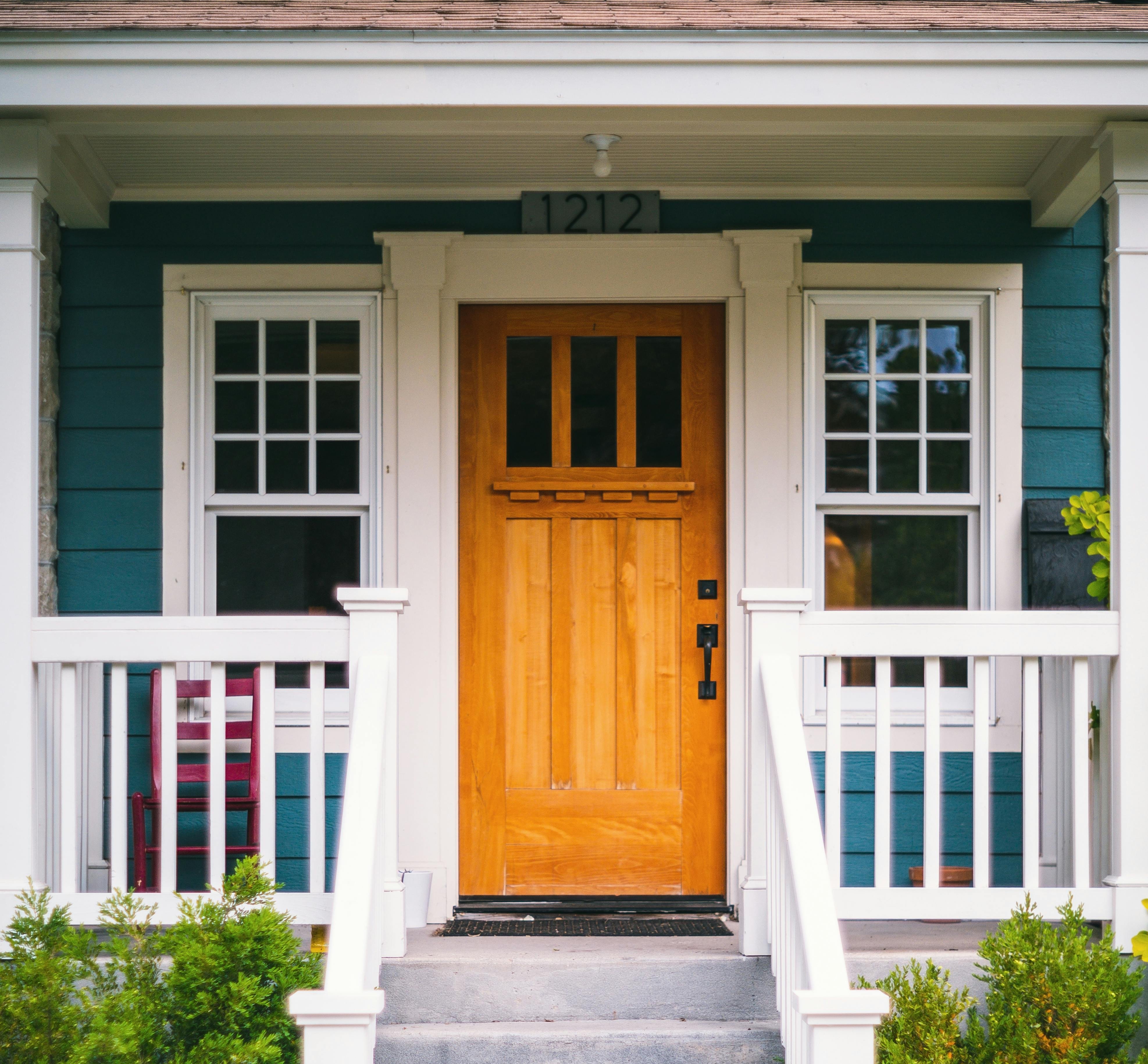 A blue and white house with a wooden door and white railings on the porch