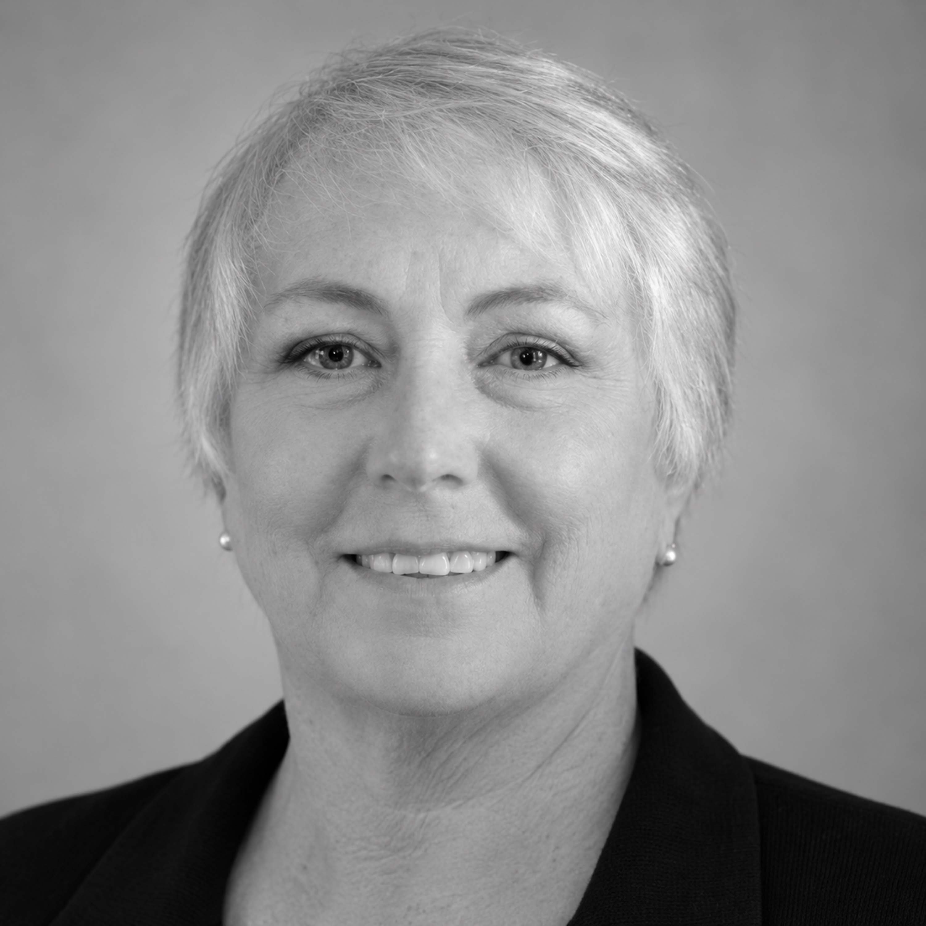 A professional headshot of a woman with short hair, wearing a black blazer, smiling at the camera