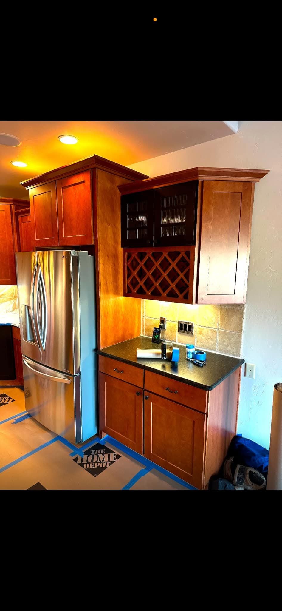 A kitchen with a stainless steel refrigerator, wooden cabinets, and a countertop with tools and a wine rack