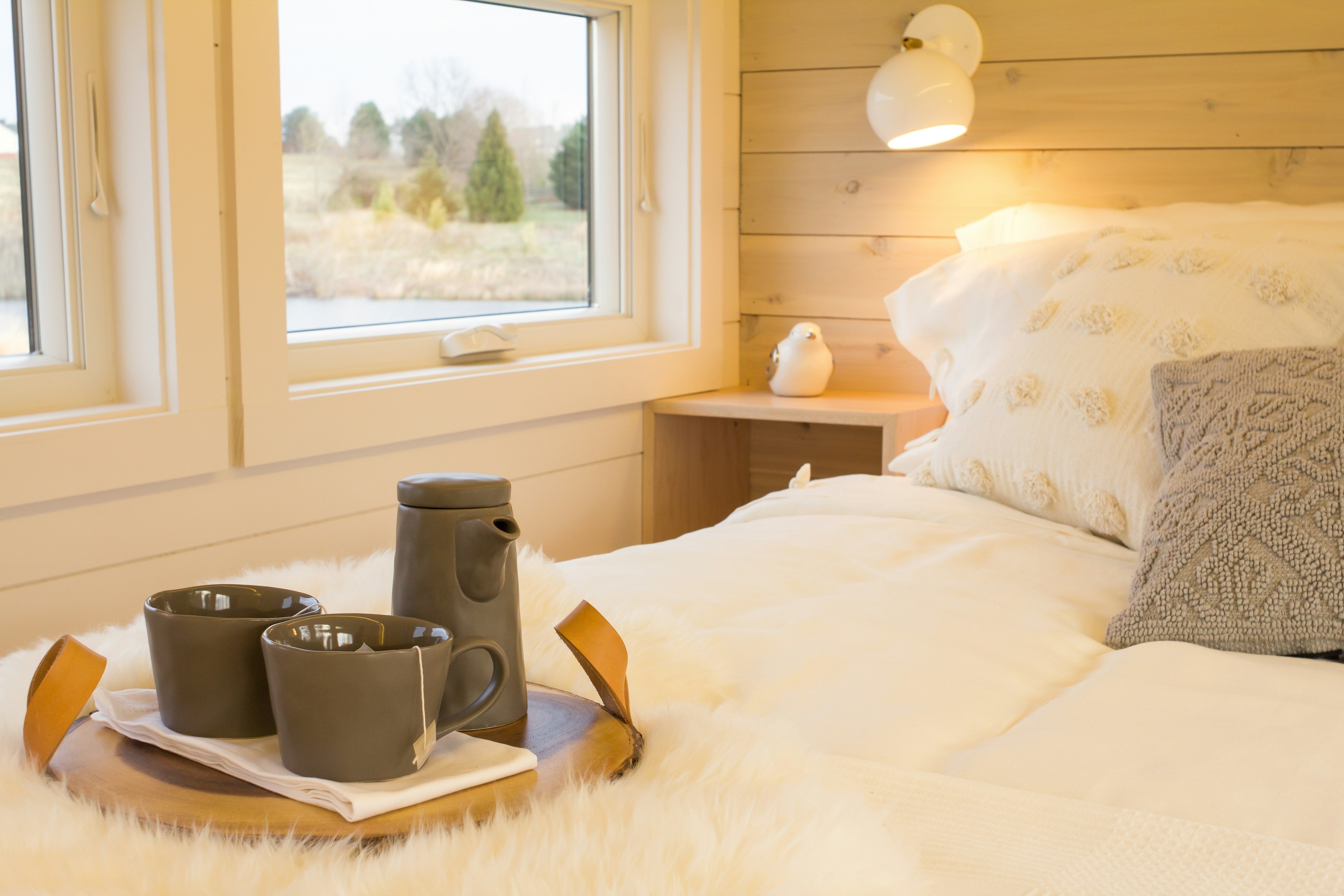 A cozy bedroom with a bed, pillows, and a tray with cups on a white fur blanket.