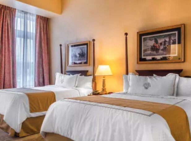Two double beds with white and gold bedding in a hotel room with yellow walls and framed pictures