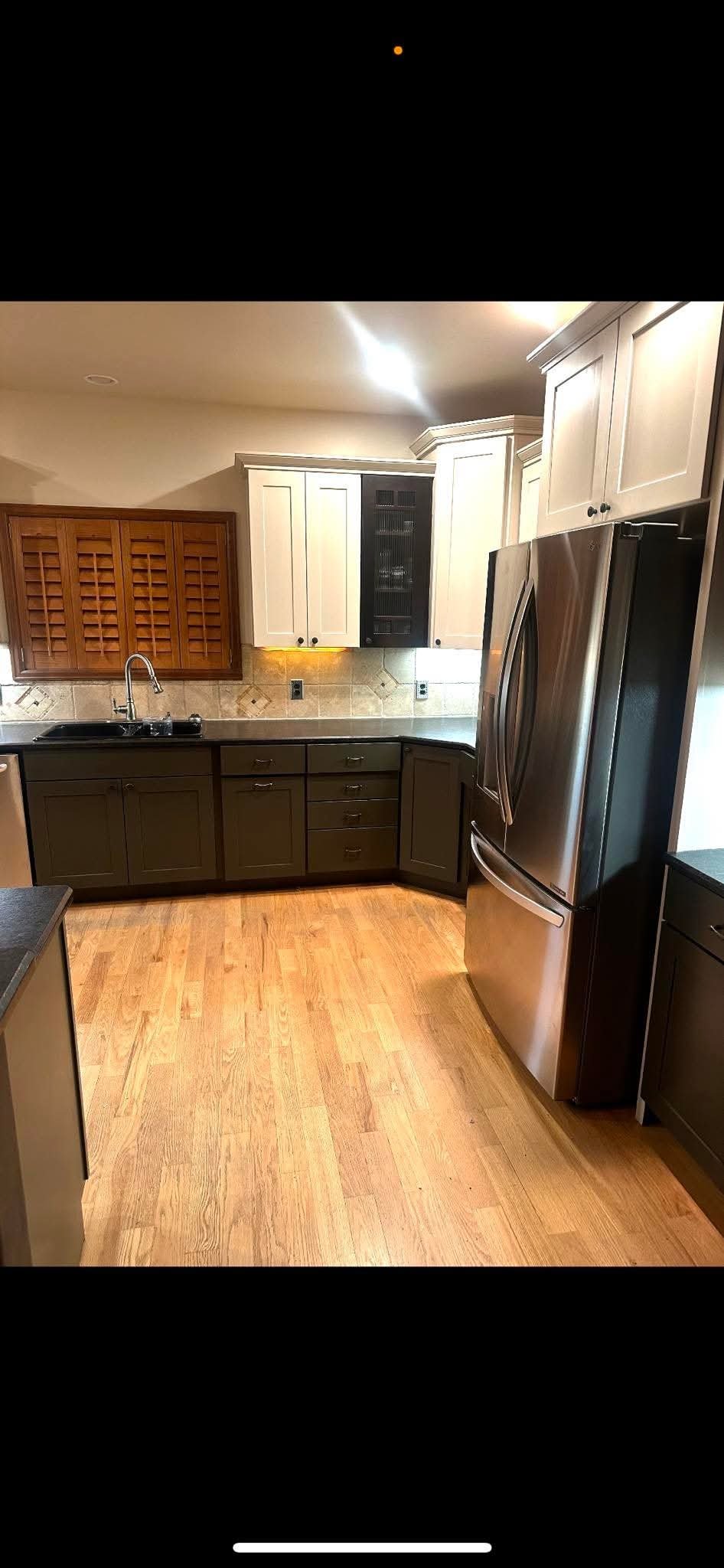 A modern kitchen with wooden floors, white cabinets, and a stainless steel refrigerator