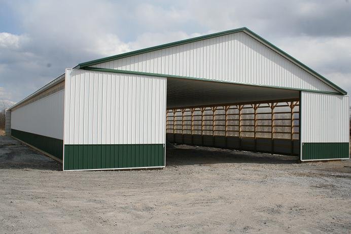 A white and green metal barn with a wooden frame and open doors under a cloudy sky
