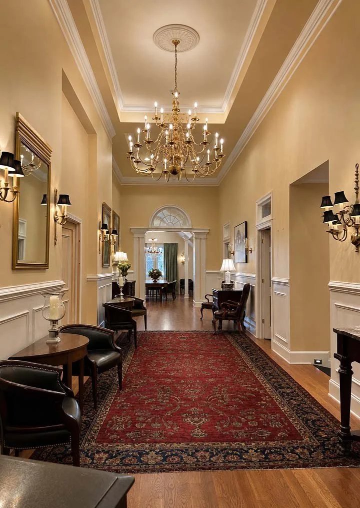 A luxurious hallway with a chandelier, a red carpet, and elegant furniture