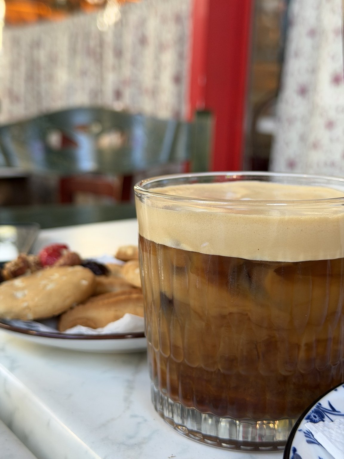 A glass of iced coffee with whipped cream on top, accompanied by a plate of cookies and pastries.