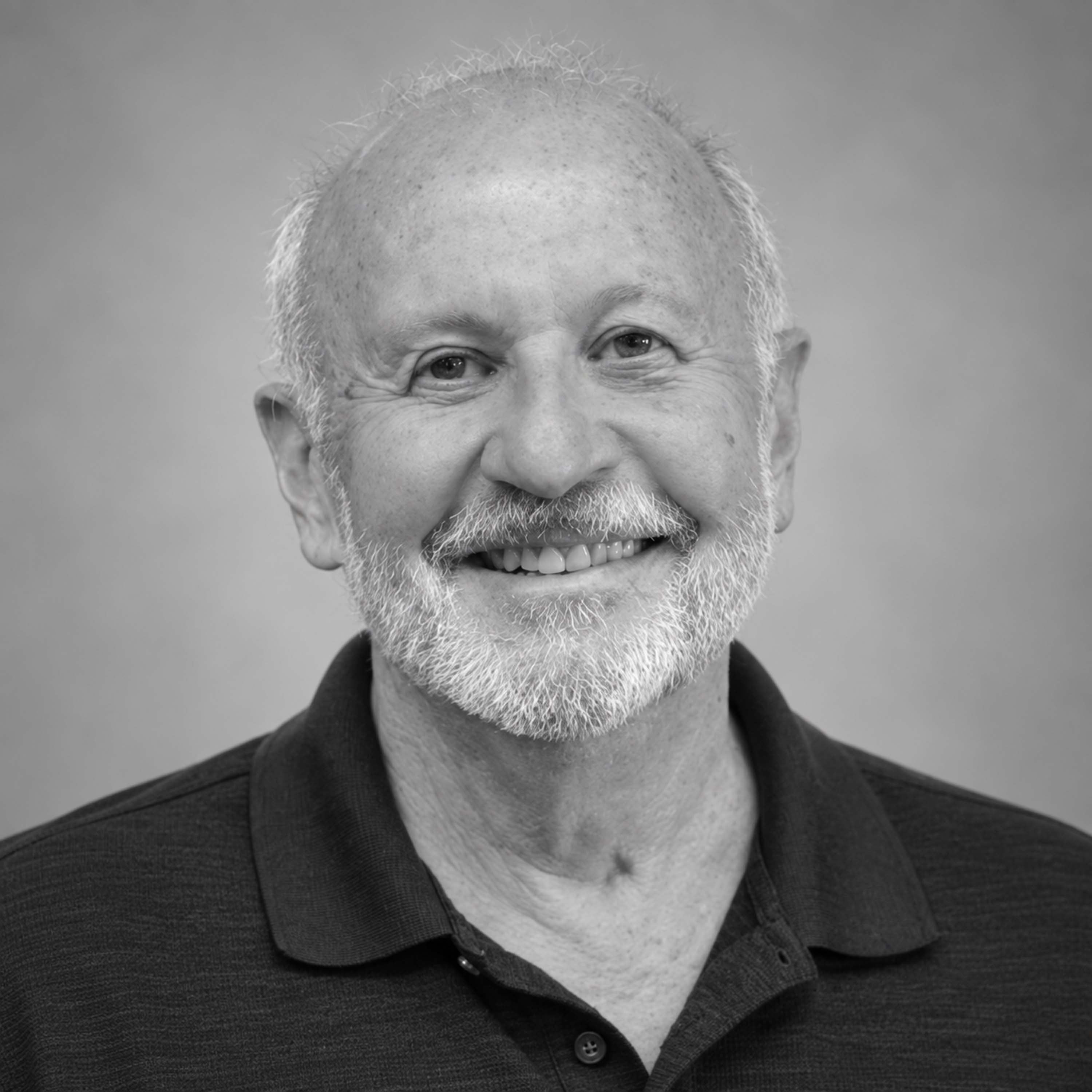 A black and white headshot of an older man with a white beard and mustache smiling