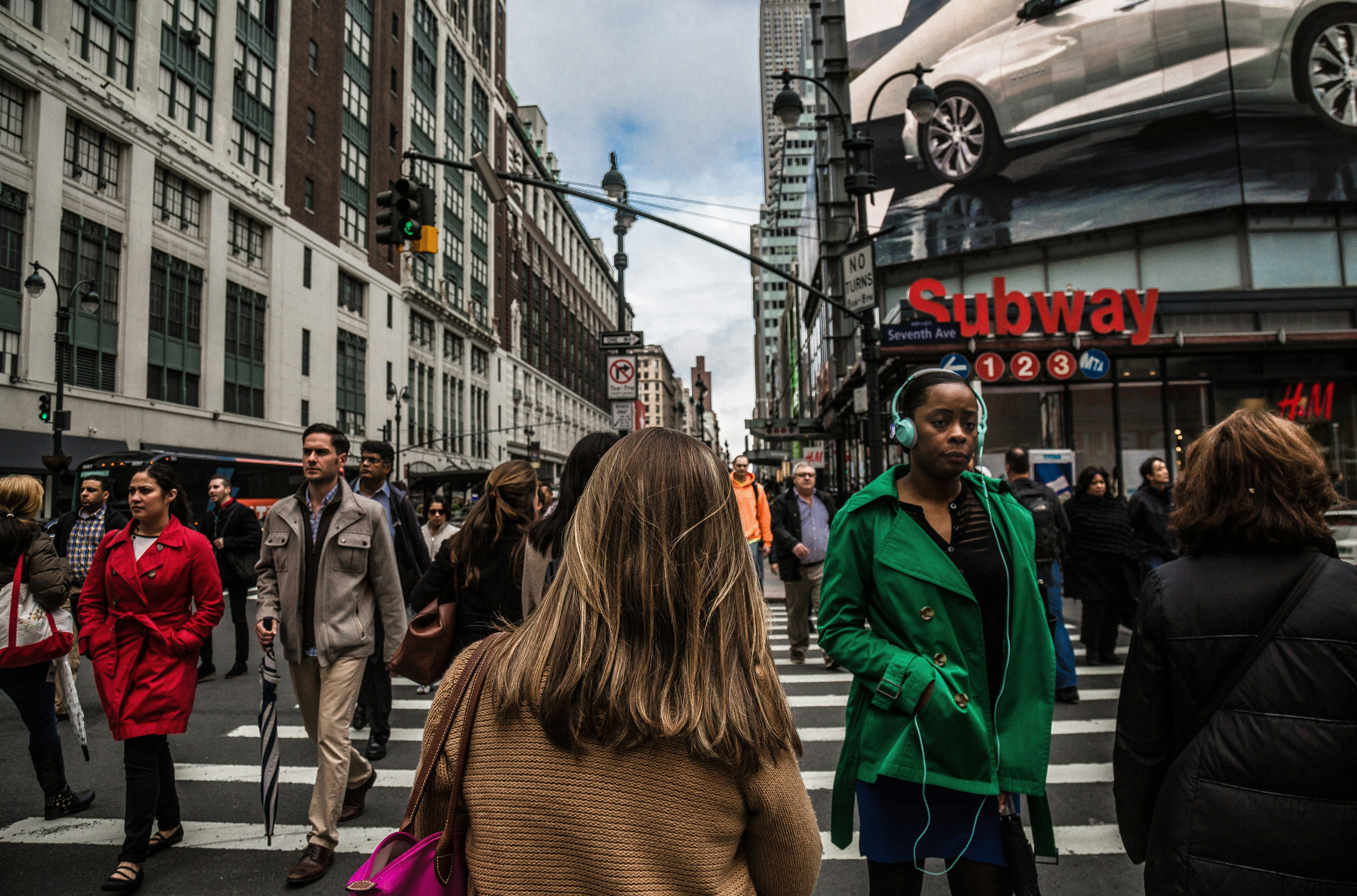 Pedestrians crossing a busy city street with a Subway advertisement in the background.