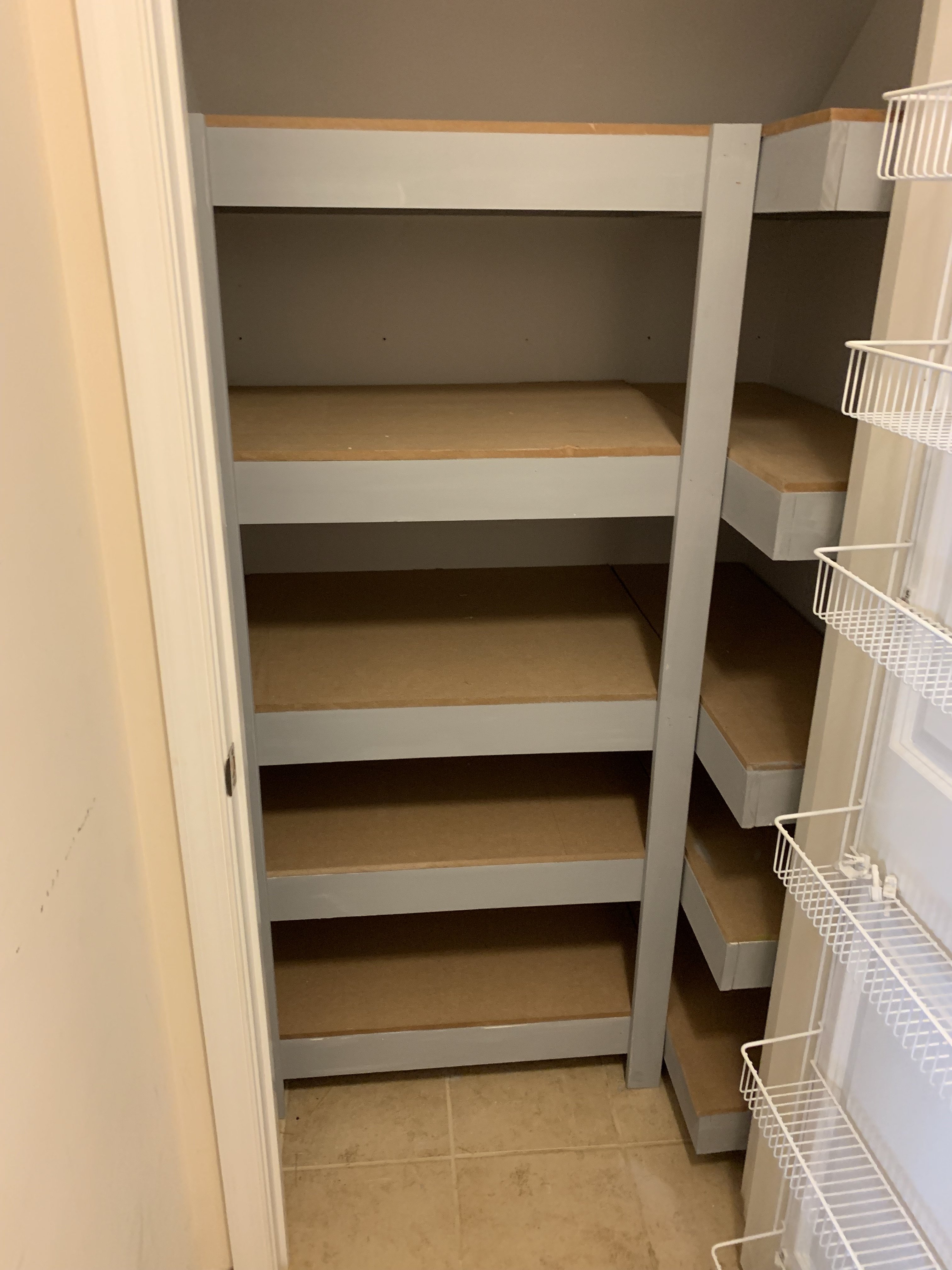 An empty pantry with wooden shelves and white wire baskets on the right side