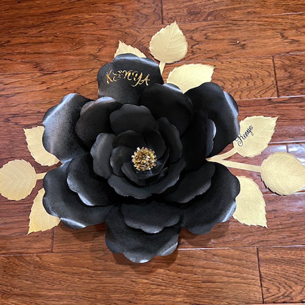 A large black paper flower with gold foil leaves and a gold center