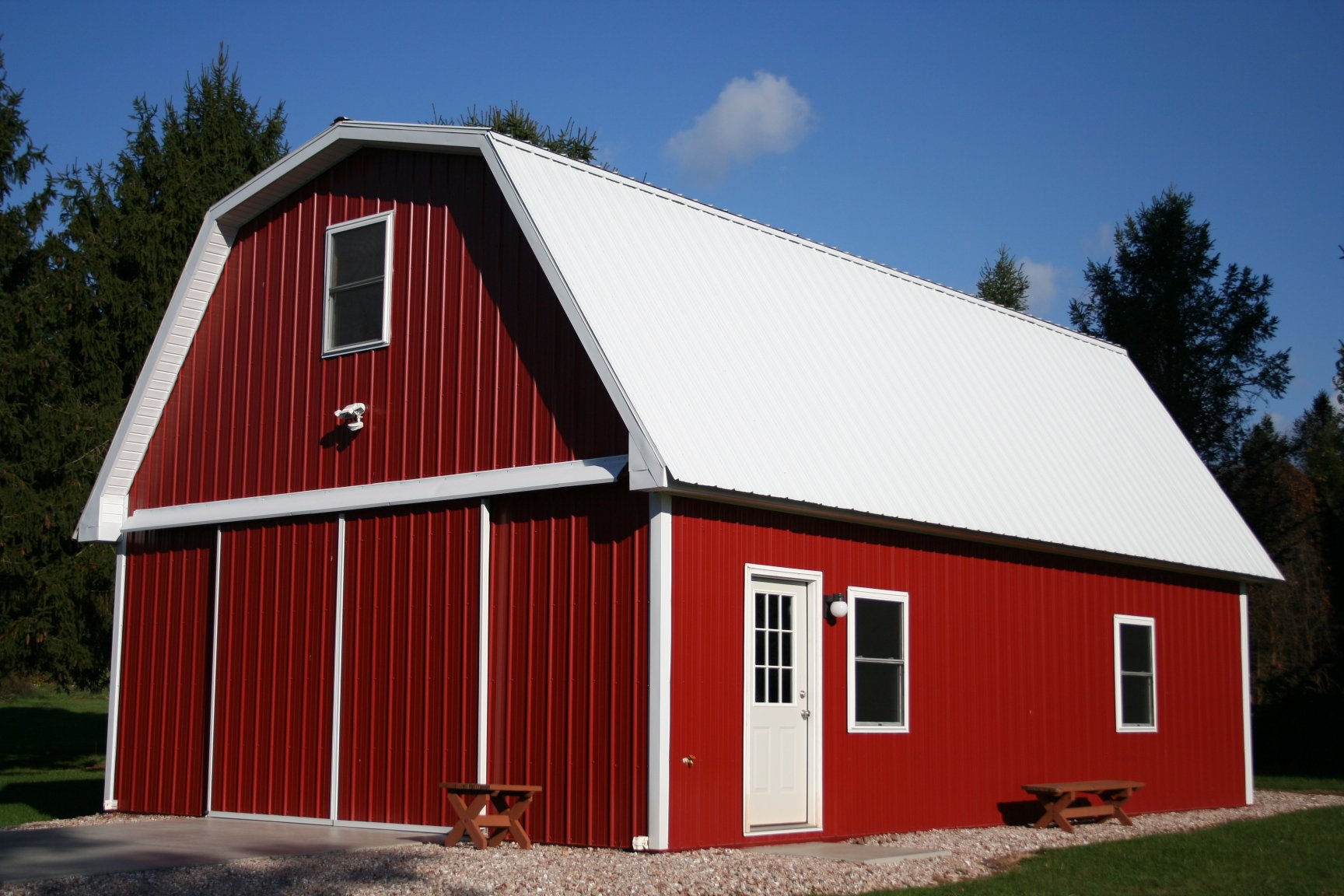 A red barn with a white roof and white trim stands in a grassy field with trees in the background.