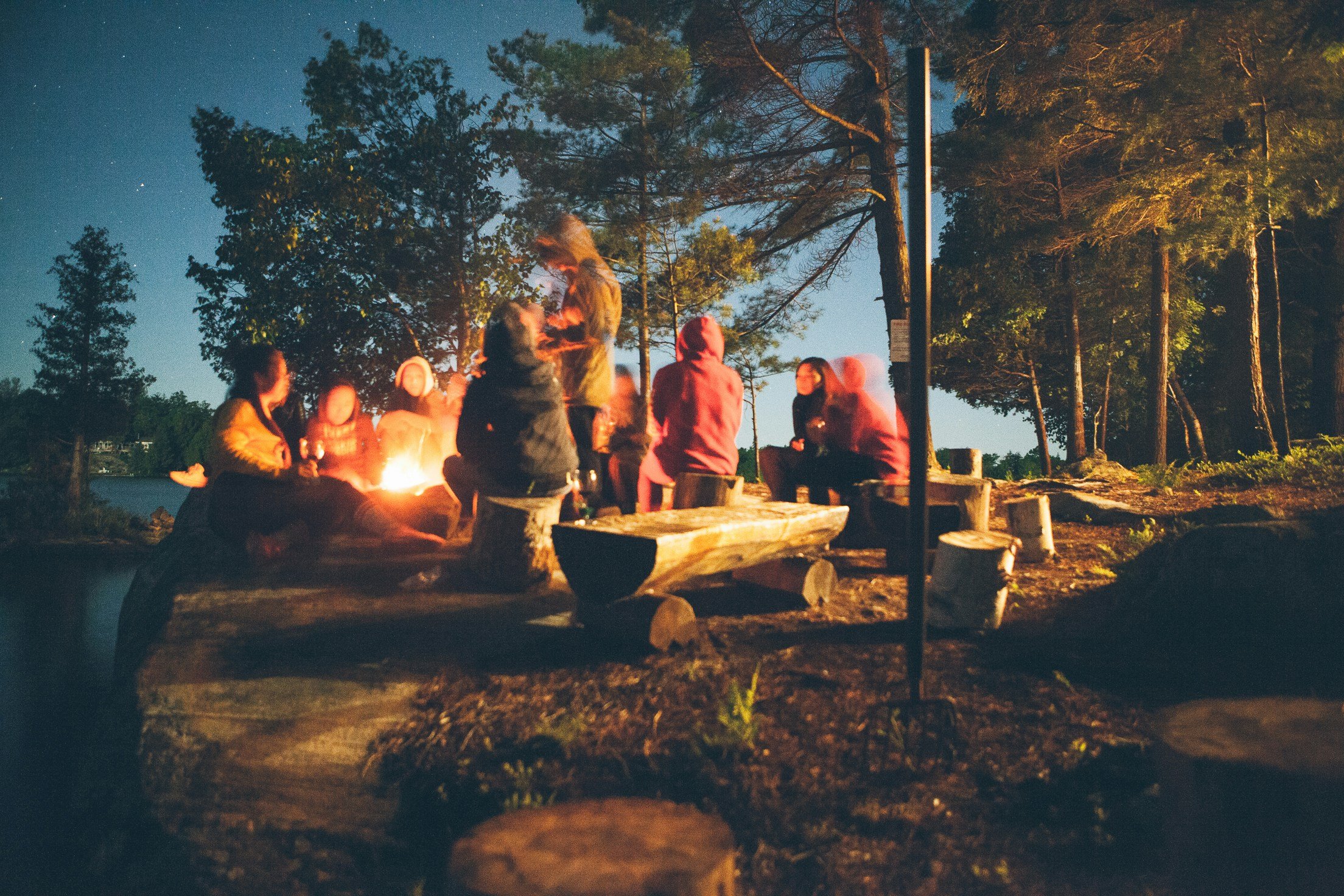 A group of people sitting around a campfire in a forest at night