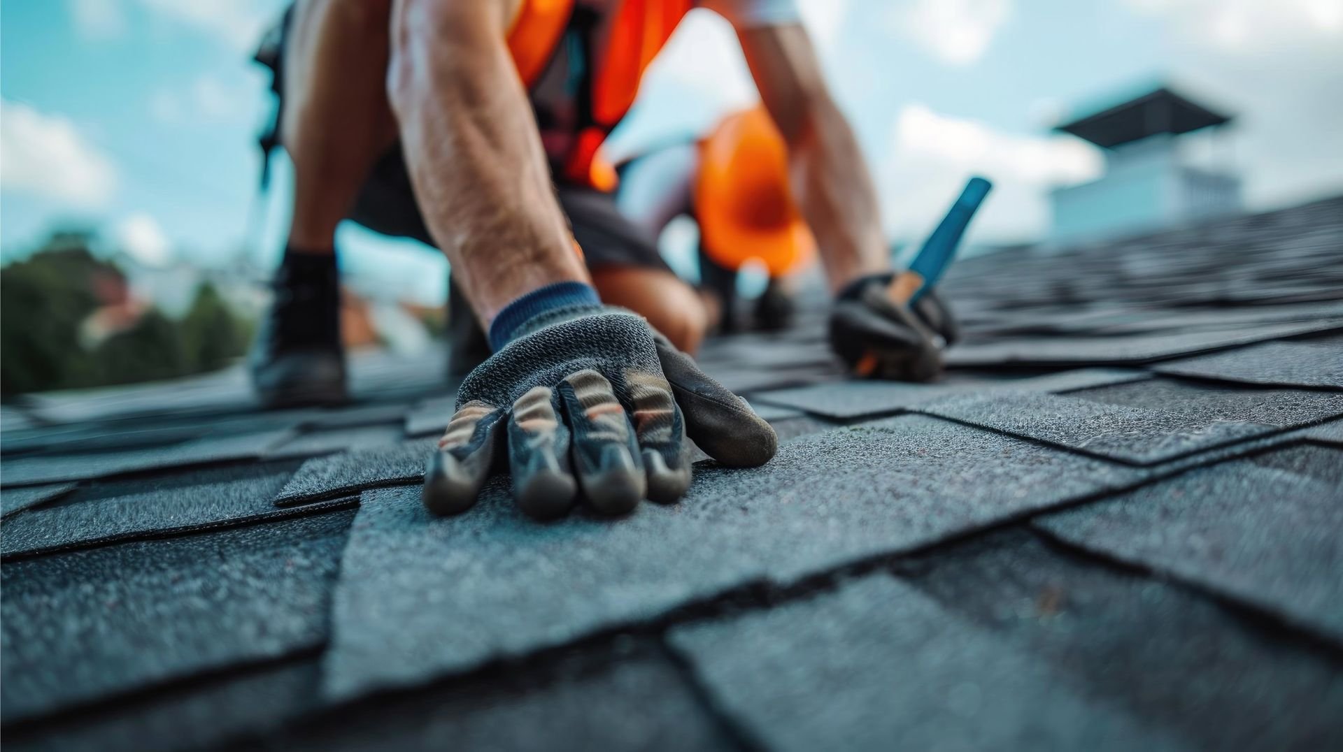 Roofer in safety gear installing asphalt shingles on a rooftop