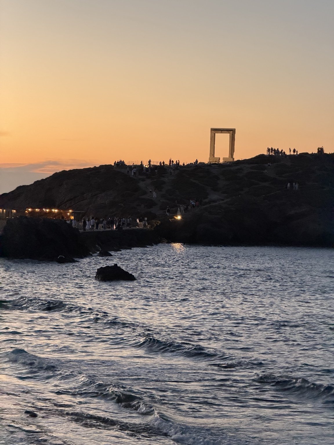 Sunset view of the Temple of Poseidon at Cape Sounion with people gathered around