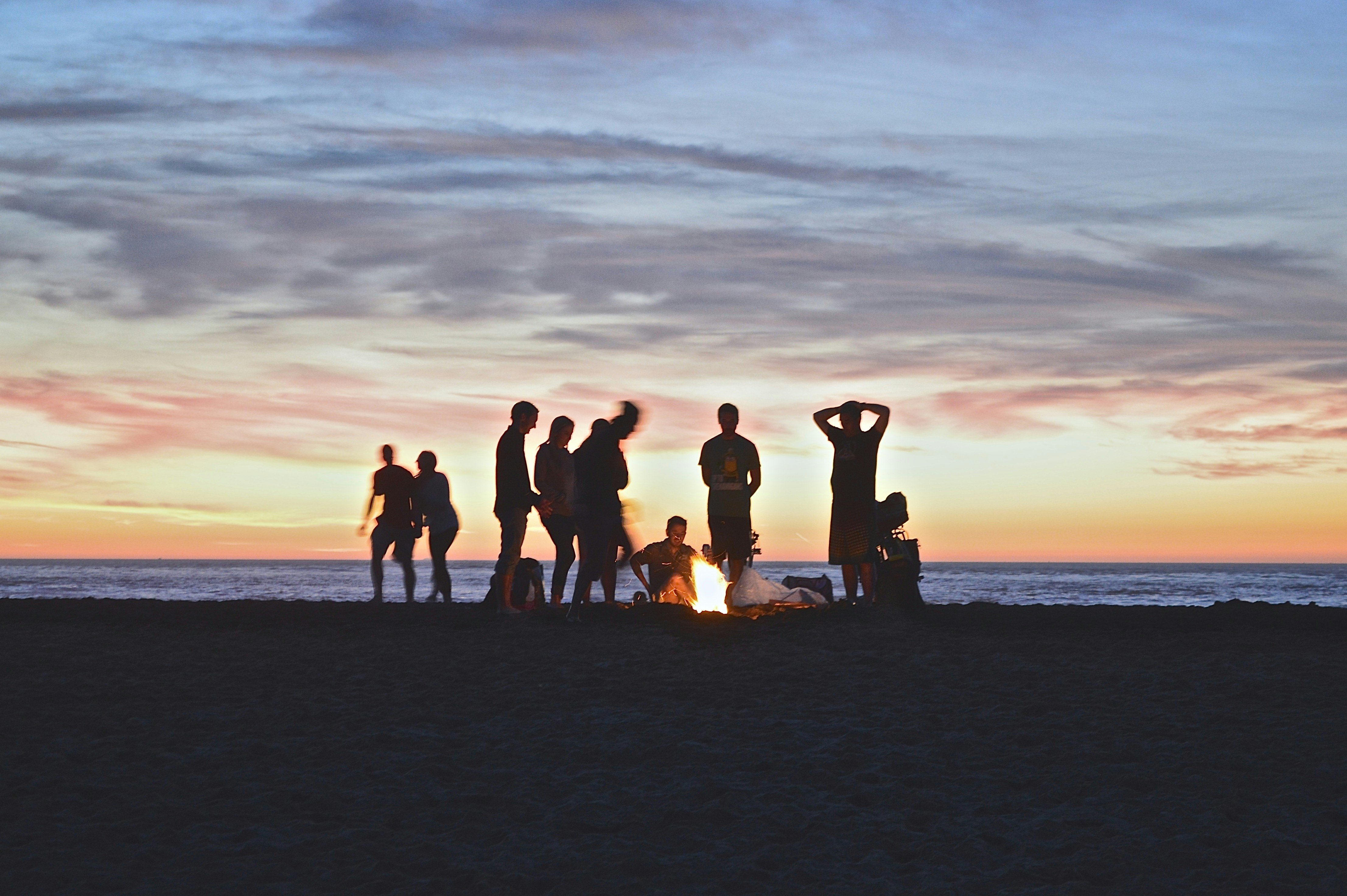 A group of people standing around a bonfire on a beach at sunset