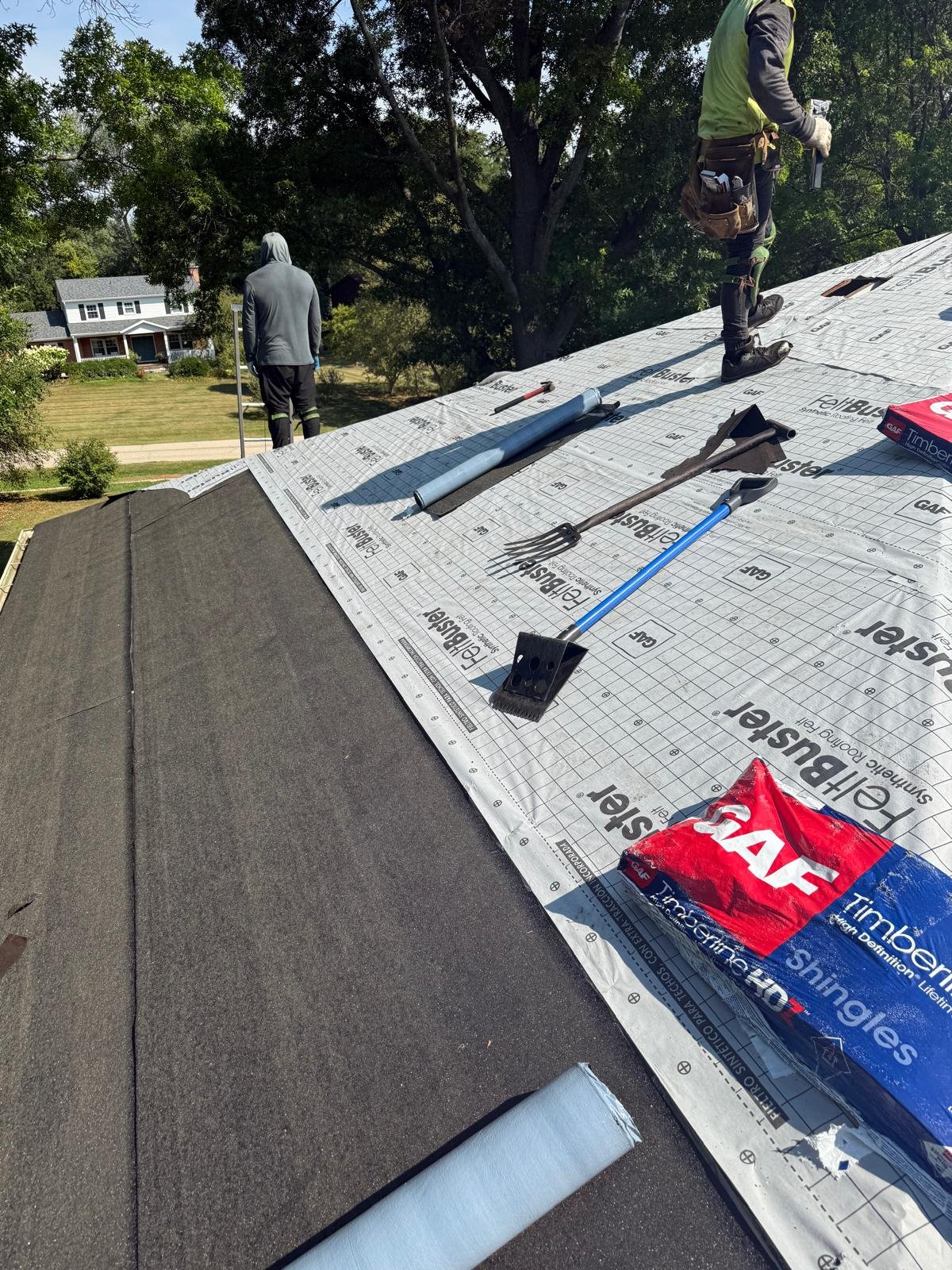 Two workers on a roof with tools and materials for a roofing project