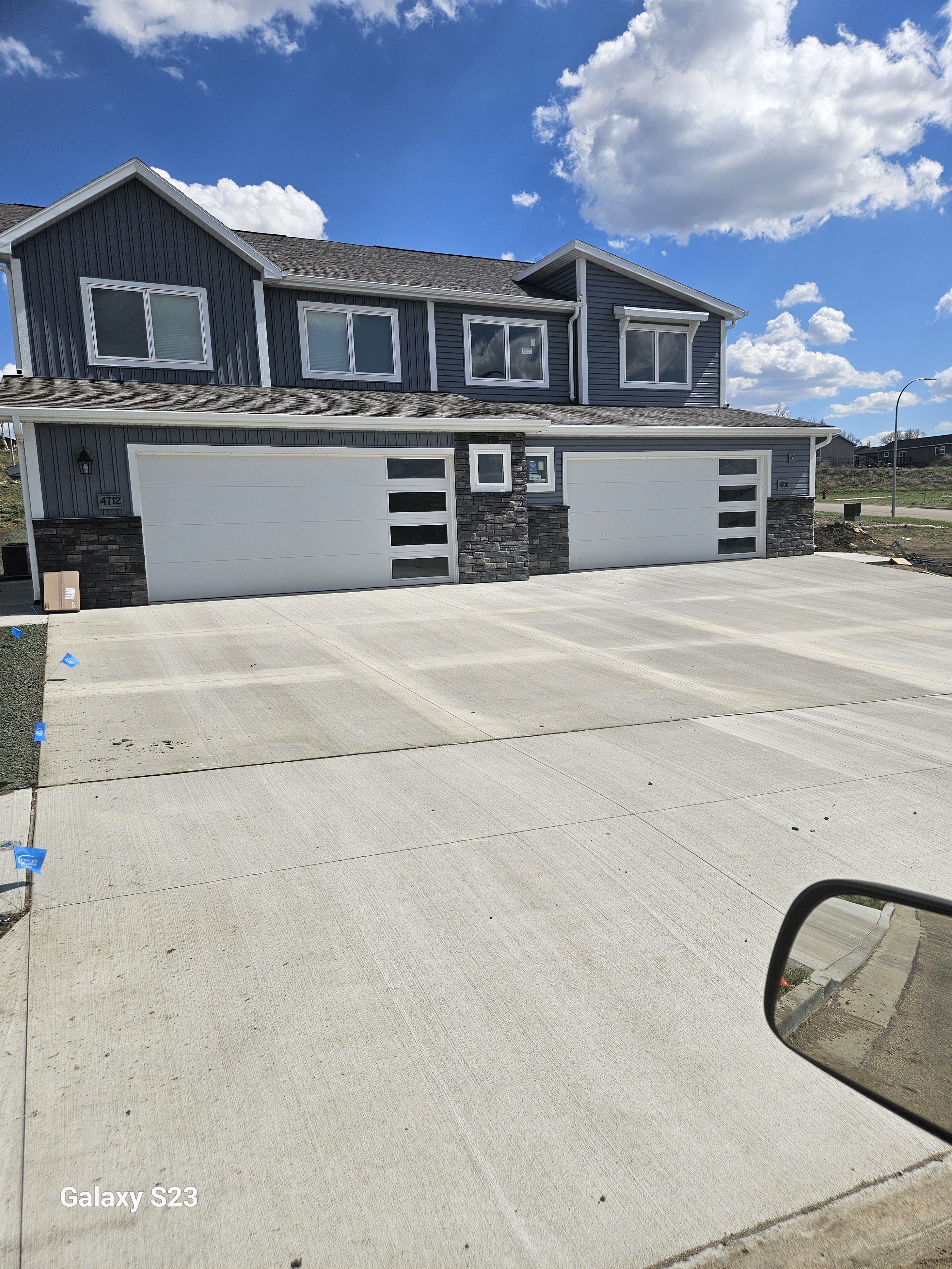 A two-story house with a gray exterior, white garage doors, and a driveway in front.