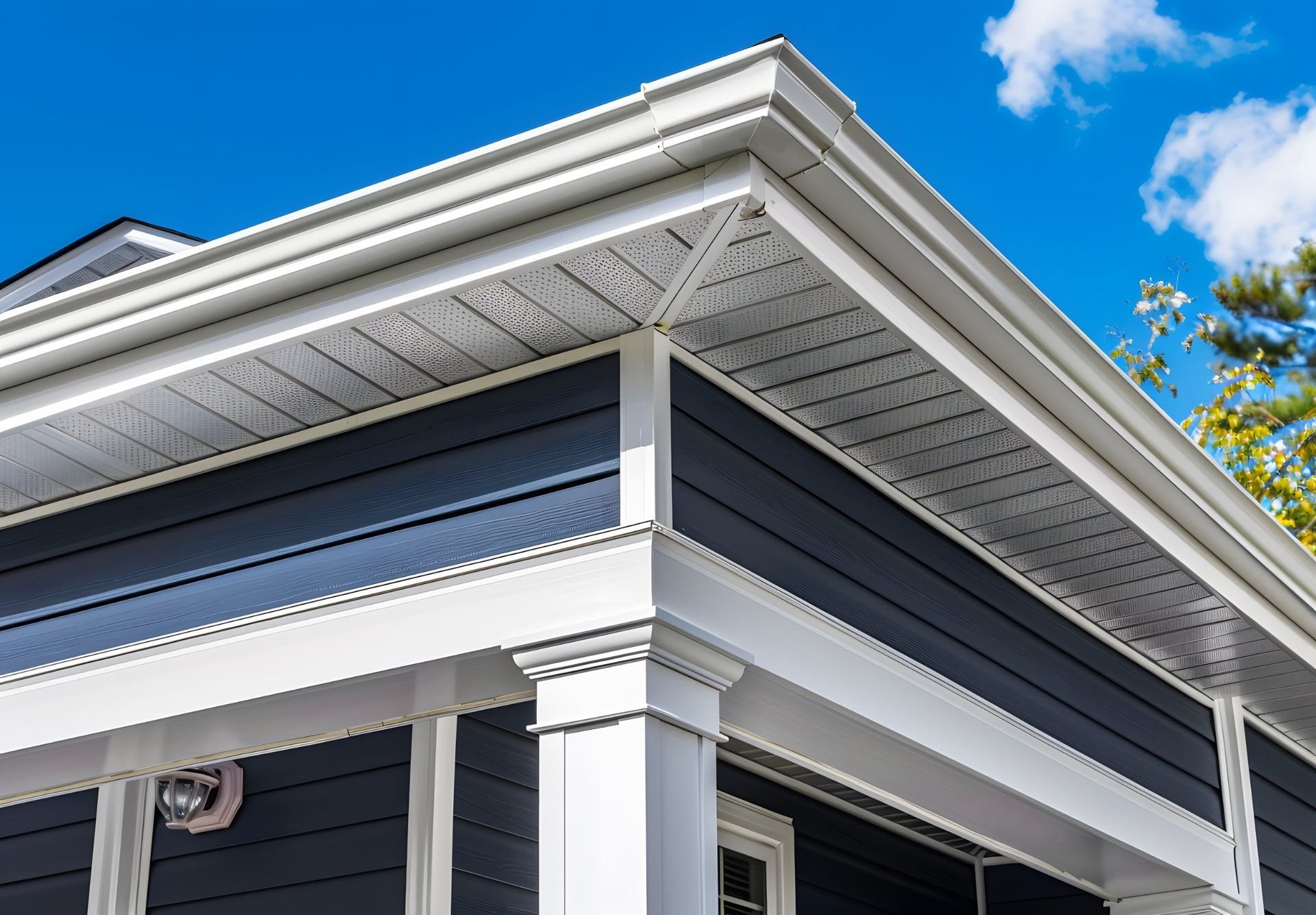 Blue house exterior with white trim, soffit, and gutters against a blue sky