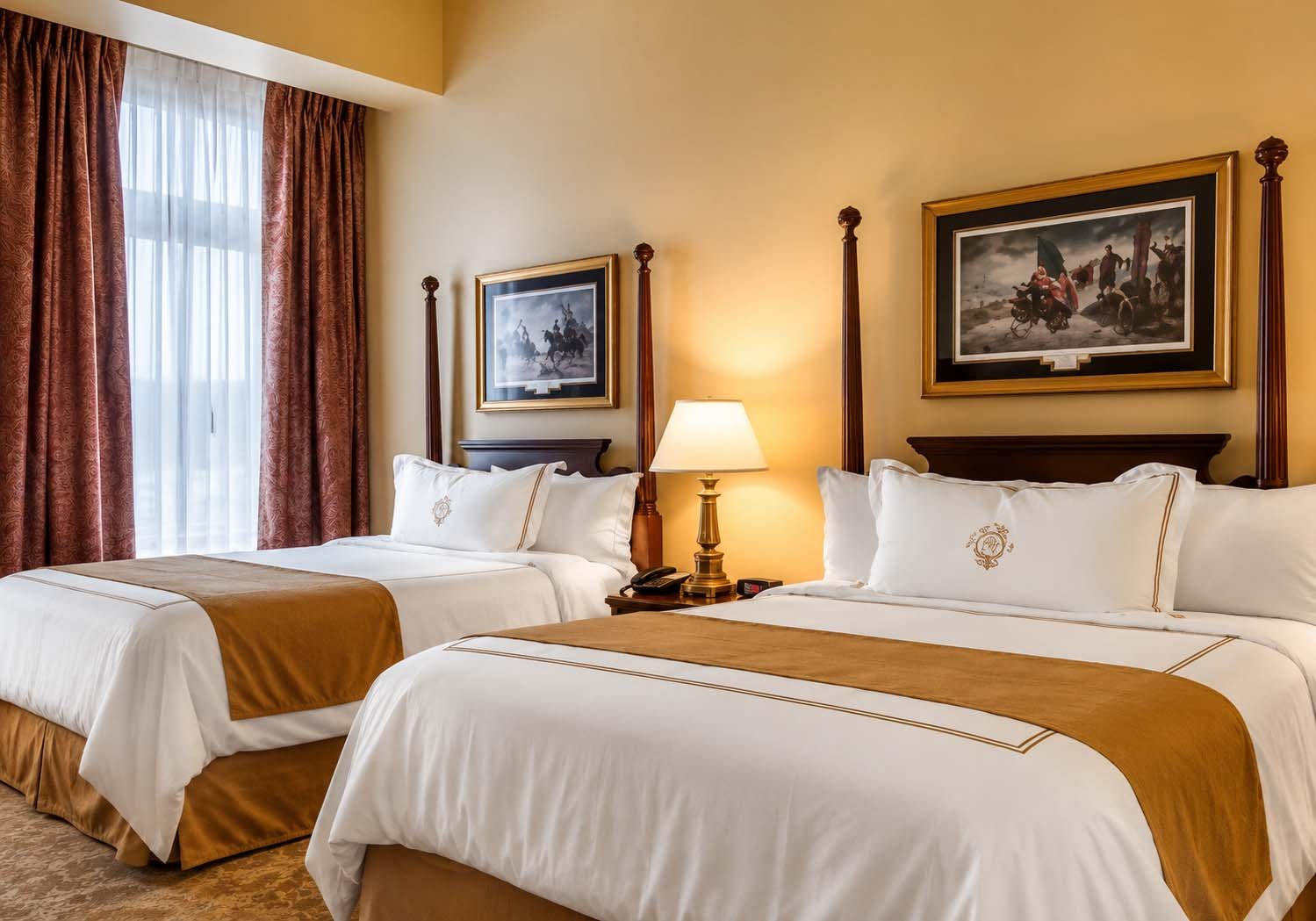 Two double beds in a hotel room with beige walls and framed pictures