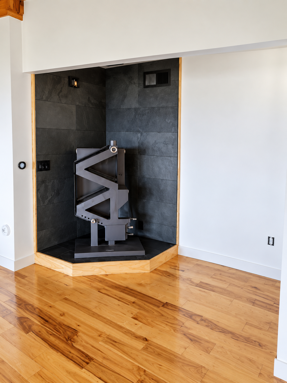 A modern fireplace with a sleek stove in a minimalist room with hardwood floors