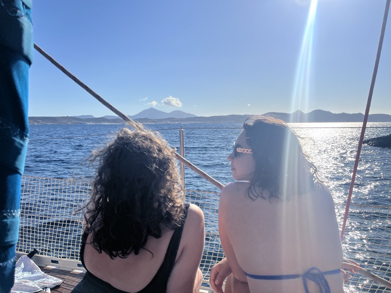 Two women sitting on a boat, looking at the sea and mountains in the distance