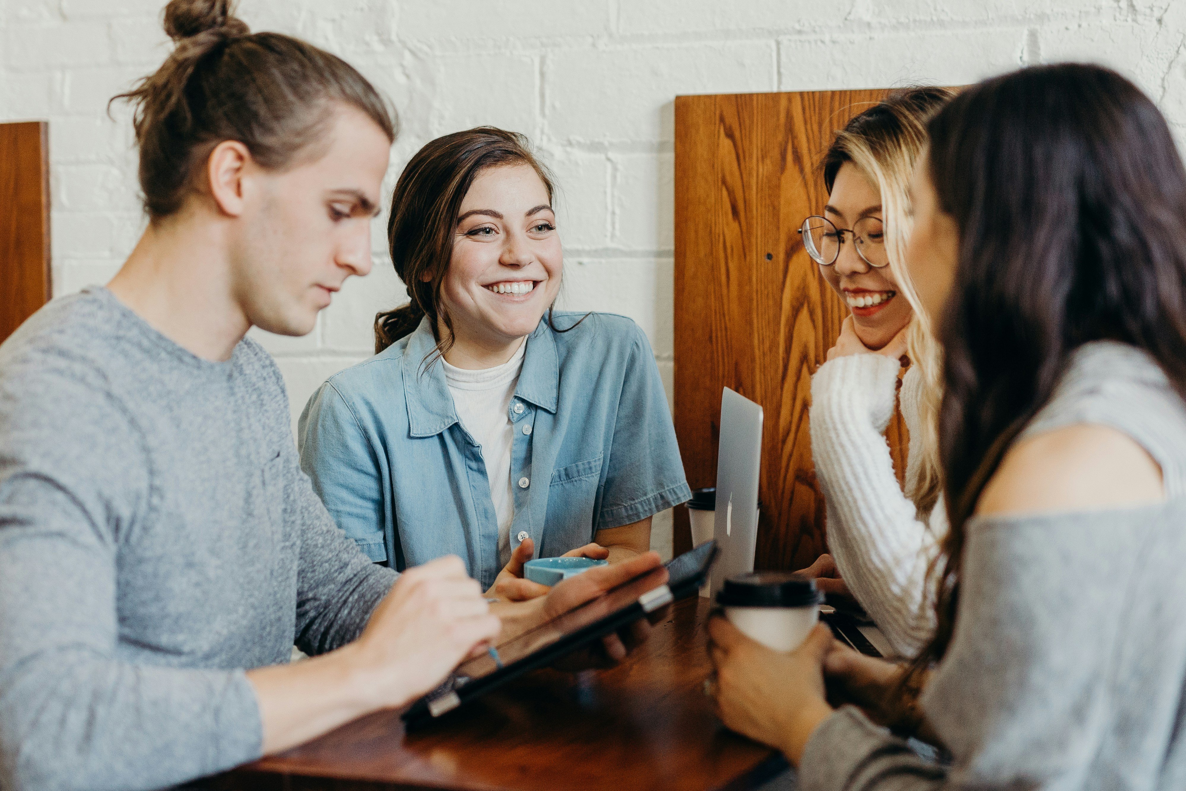 Four young adults sitting at a table, smiling and looking at a tablet