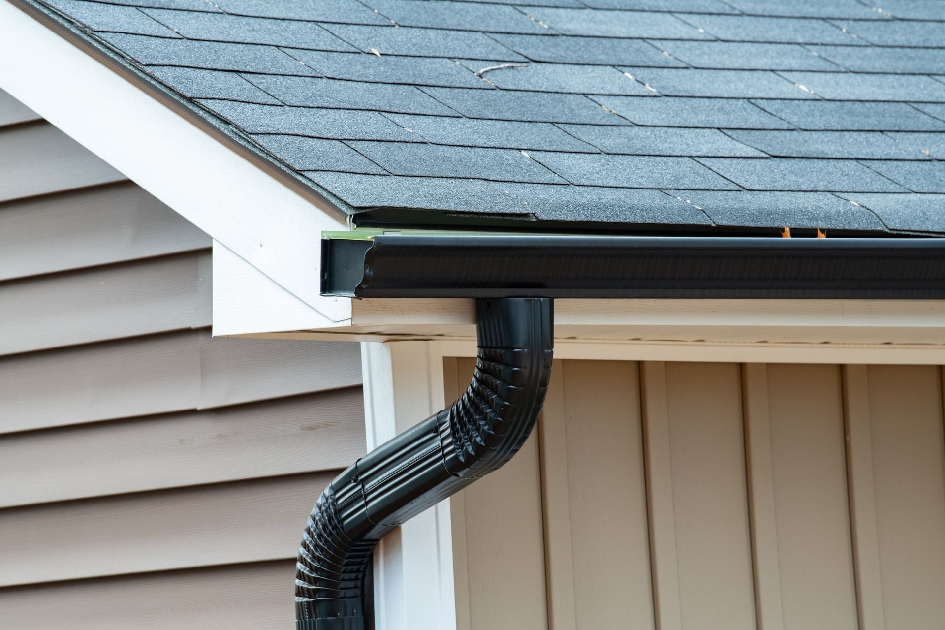 Black rain gutter attached to a light-colored house with a dark roof