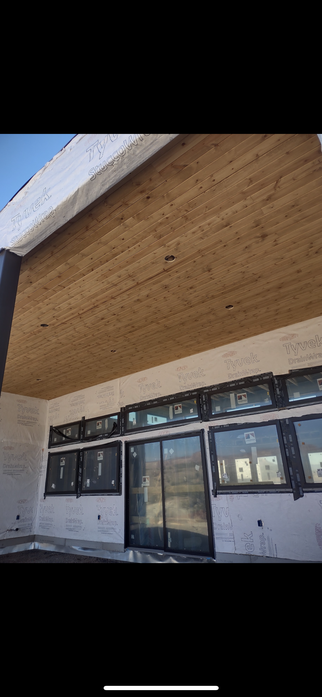 A construction site with a wooden ceiling and glass windows under a blue sky